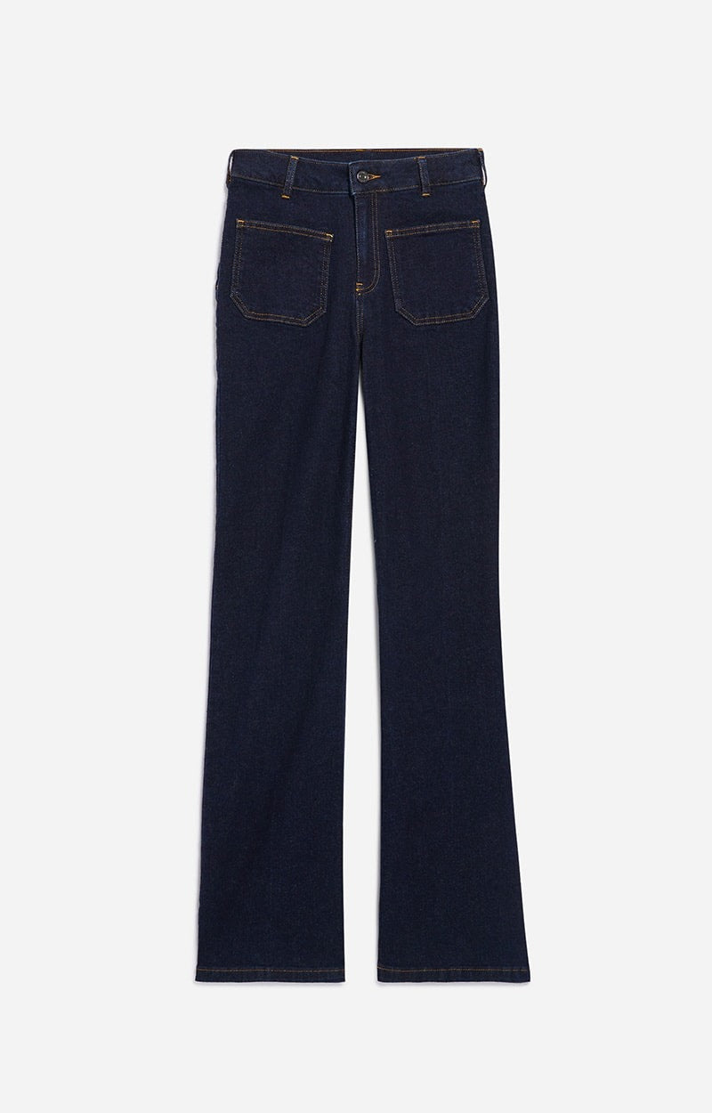 A pair of Vanessa Bruno Dompay Flare Jeans is displayed flat against a white background. Inspired by 70's flair, these dark blue denim jeans feature a classic straight-leg cut with two front pockets, two back pockets, belt loops, and a button with a zipper closure. The visible stitching contrasts in a golden color.