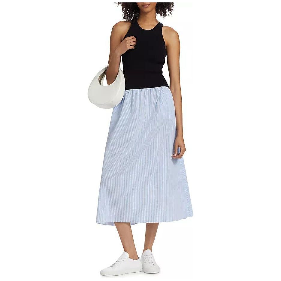 A woman is wearing the Naadam Mixed Media Midi Dress in a Black Blue Combo. She is carrying a white, crescent-shaped handbag on her shoulder and wearing white sneakers. With curly hair, she poses against a plain background.