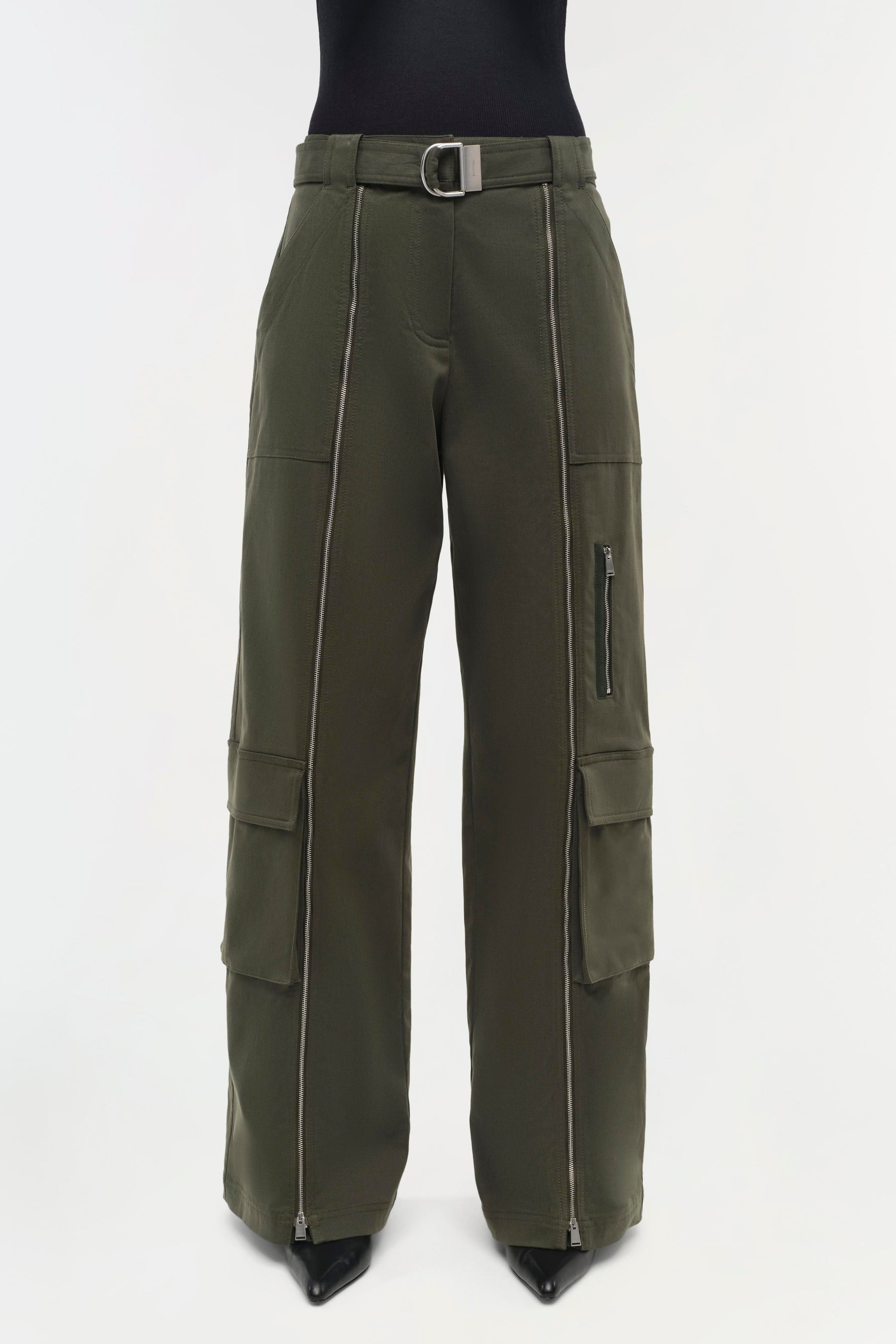 A pair of Simkhai Fabiana Belted Pants in Moss, boasting a high waist and a coordinating belt with a rectangular metallic buckle. These stylish cargo pants feature a front zipper fly, multiple pockets, and zipper details running down the front of each leg. The wide legs extend gracefully to the ankles.