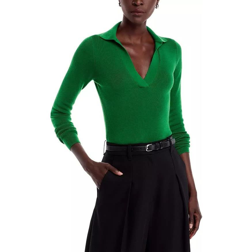 A person wearing the Vanessa Bruno Dorita Top in bright green, featuring long sleeves, soft cotton material, and a V-neck design, is shown with a black belt and their hand in the pocket of black high-waisted pants against a white background.