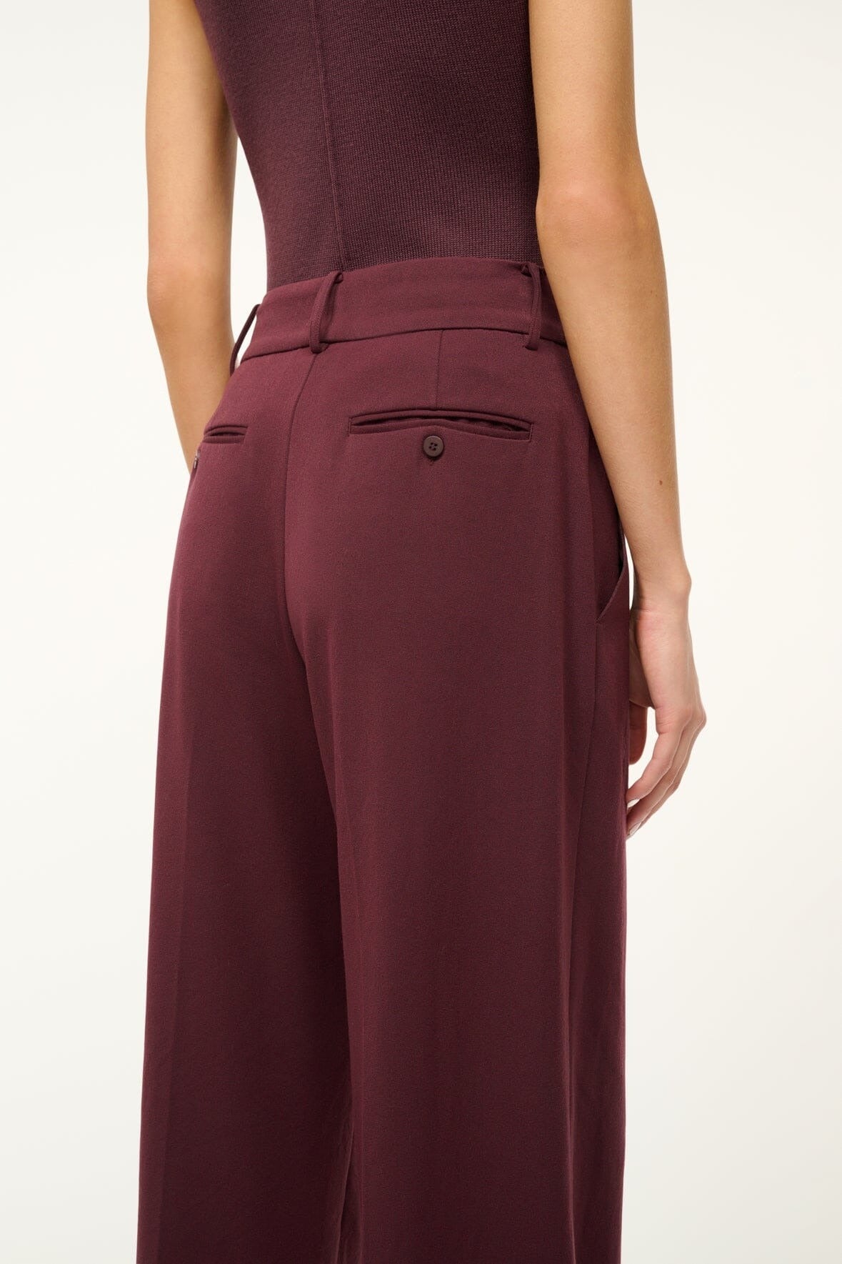 A person is seen from behind wearing the Staud Prince Pant Merlot by Staud, featuring burgundy flat front wide-leg pants with two back welt pockets and a matching sleeveless top against a plain light-colored background.