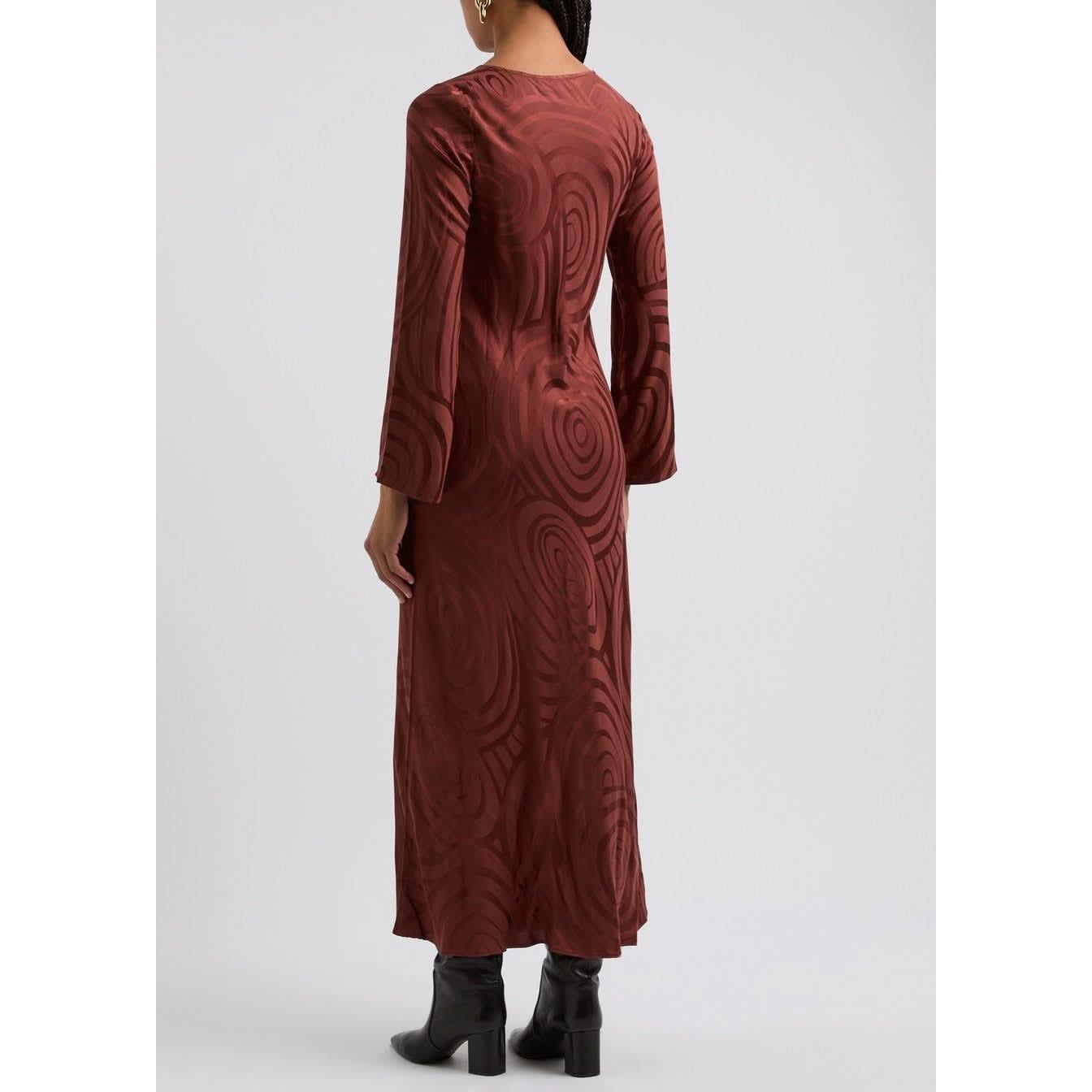 A person is standing with their back to the camera, showcasing a long-sleeved, ankle-length Rixo Alondra Dress Whirlpool Jacquard Merlot. They are wearing black boots and have long hair, against a plain white background.