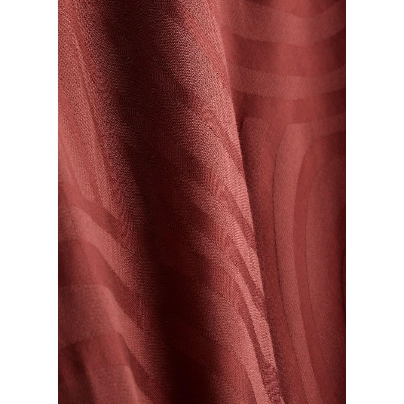 Close-up of the Whirlpool Jacquard Merlot fabric from the Rixo Alondra Dress. This textured material features a wavy pattern in a rich, reddish-brown color. The fabric has a subtle sheen, reminiscent of luxurious silk crepe de chine. The smoothly flowing lines create depth and movement, while the lighting enhances its undulating design.