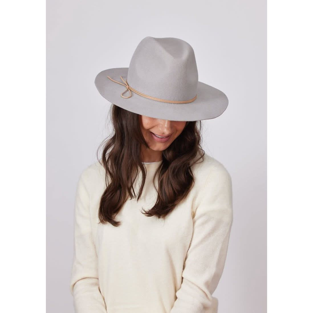 A person wearing the Hat Attack Classic Amelia in light gray, paired with a cream-colored sweater, looks down. Their long brown hair cascades over their shoulders against a plain white background, highlighting the timeless elegance of Hat Attack's hats made in the USA.