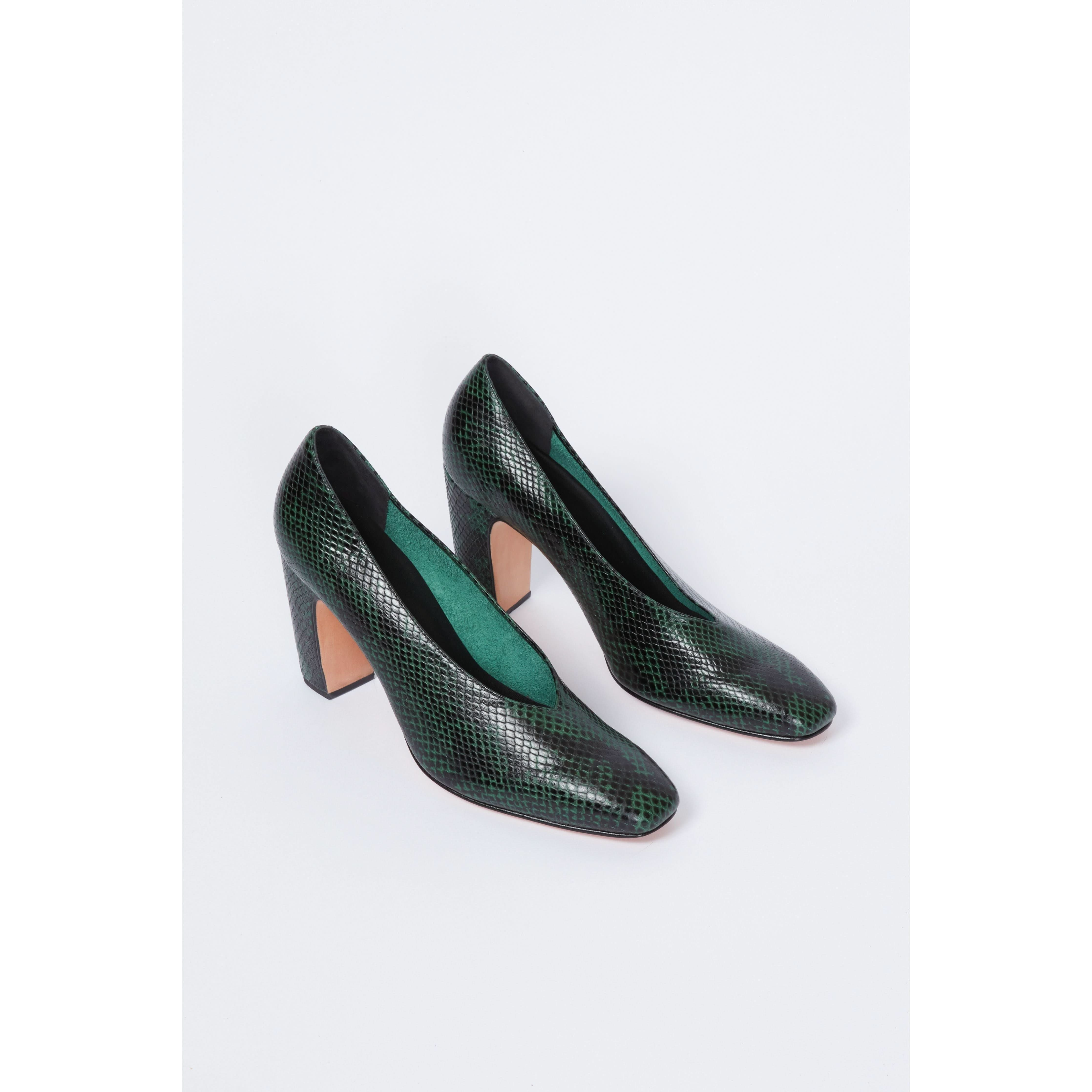 The Rachel Comey Chloris Pump in green showcases a textured pattern reminiscent of snakeskin atop its dark green exterior. This pair features a chunky block heel and an almond-toe design, all displayed on a plain white background.