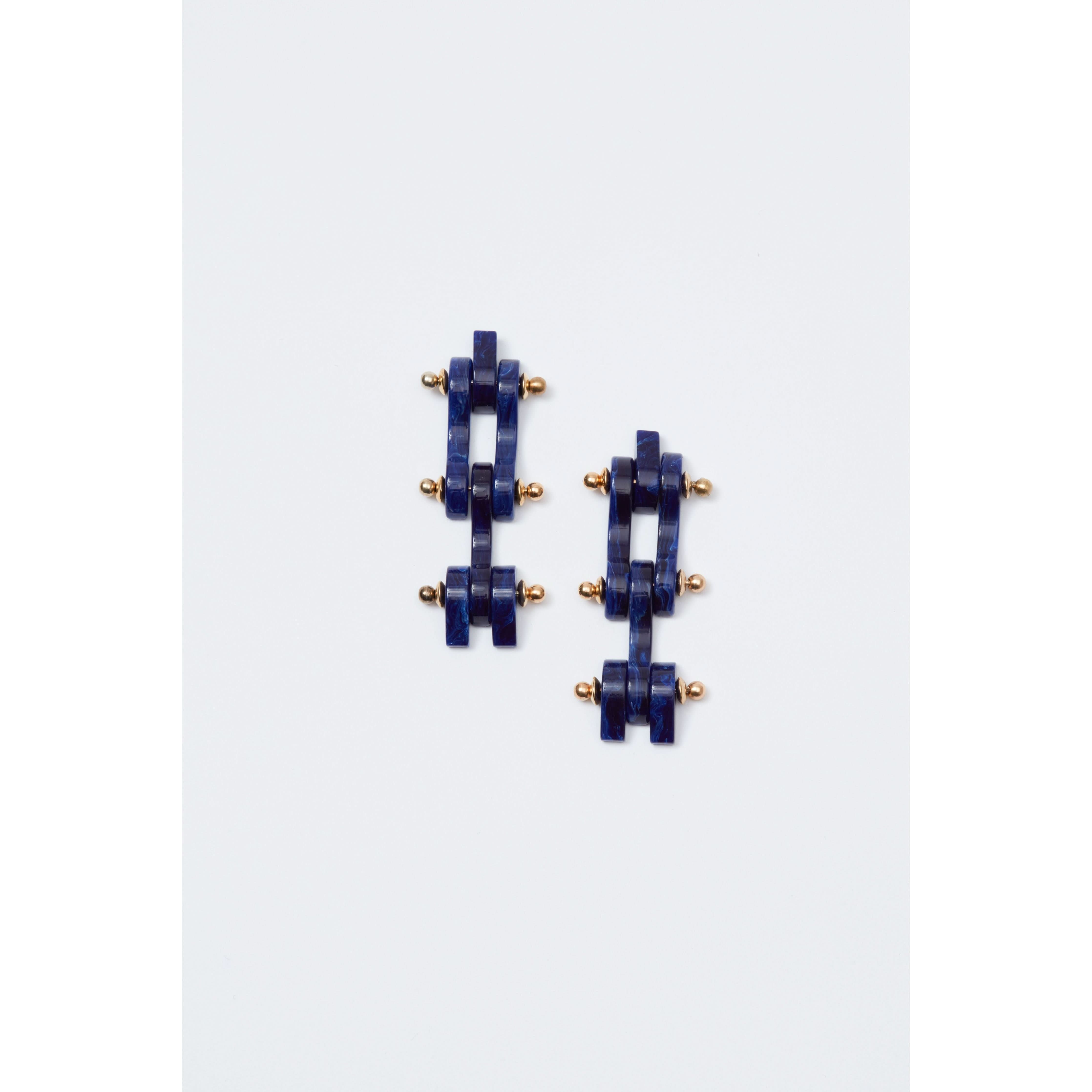 The Rachel Comey Bedford Earrings in Lapis feature a geometric design with navy blue blocks and small gold spheres arranged in an alternating pattern. Crafted with surgical steel backs, these stylish pieces exemplify exceptional craftsmanship and elegance, embodying the renowned artistry of being made in Italy.