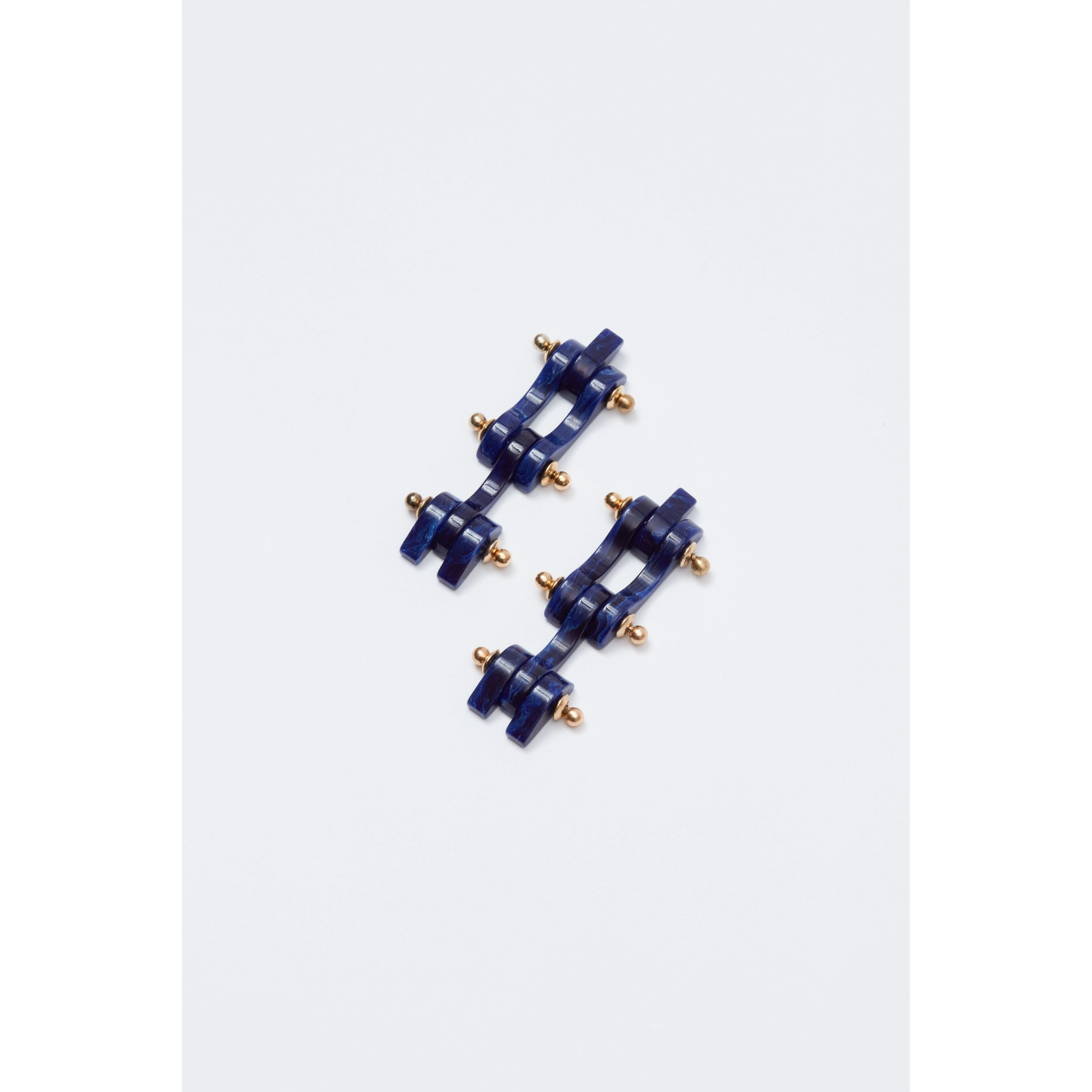 The Rachel Comey Bedford Earrings in Lapis feature a blue geometric design with multiple ridges and small gold spherical accents, crafted from surgical steel, beautifully arranged against a plain white background.