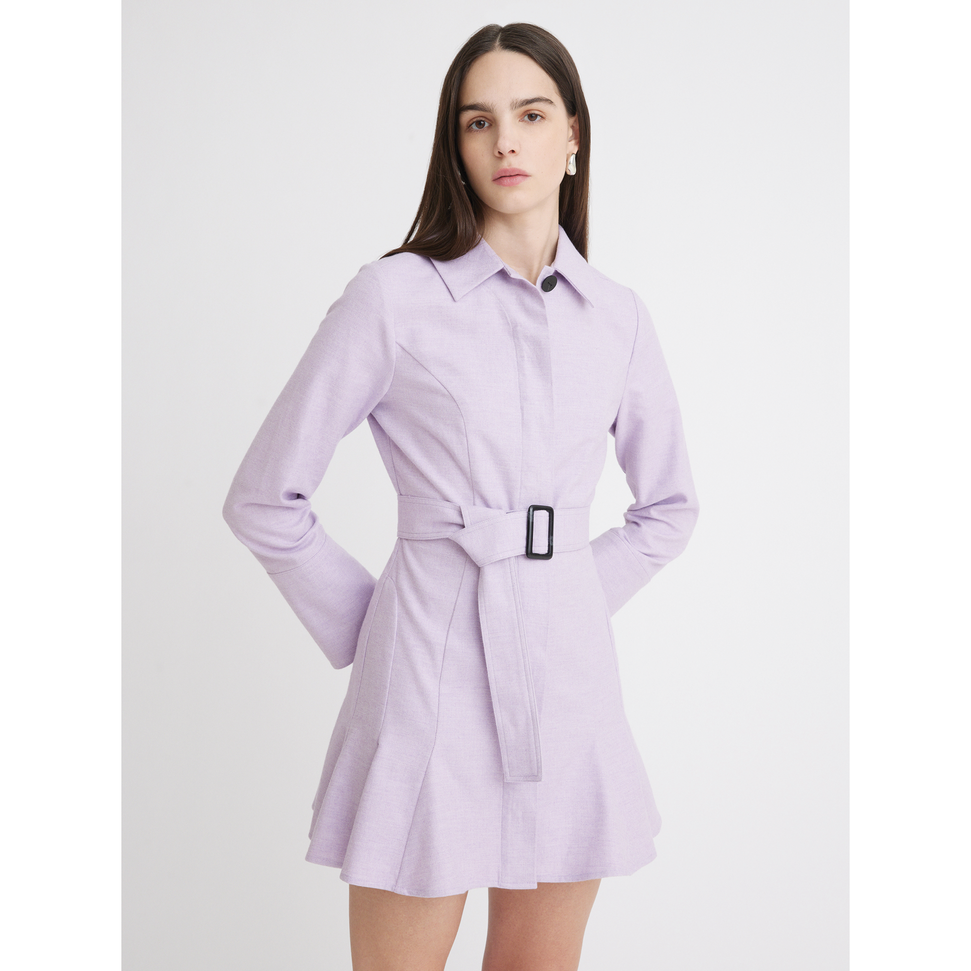 A woman with long, dark hair stands against a white background. She is wearing the Matthew Bruch Long Sleeve Mini Shirt Dress in Lavender Flannel, featuring a collar and flared hem. Made in the USA from 100% cotton, this belted dress flows elegantly as she maintains a neutral expression and keeps her hands relaxed by her sides.