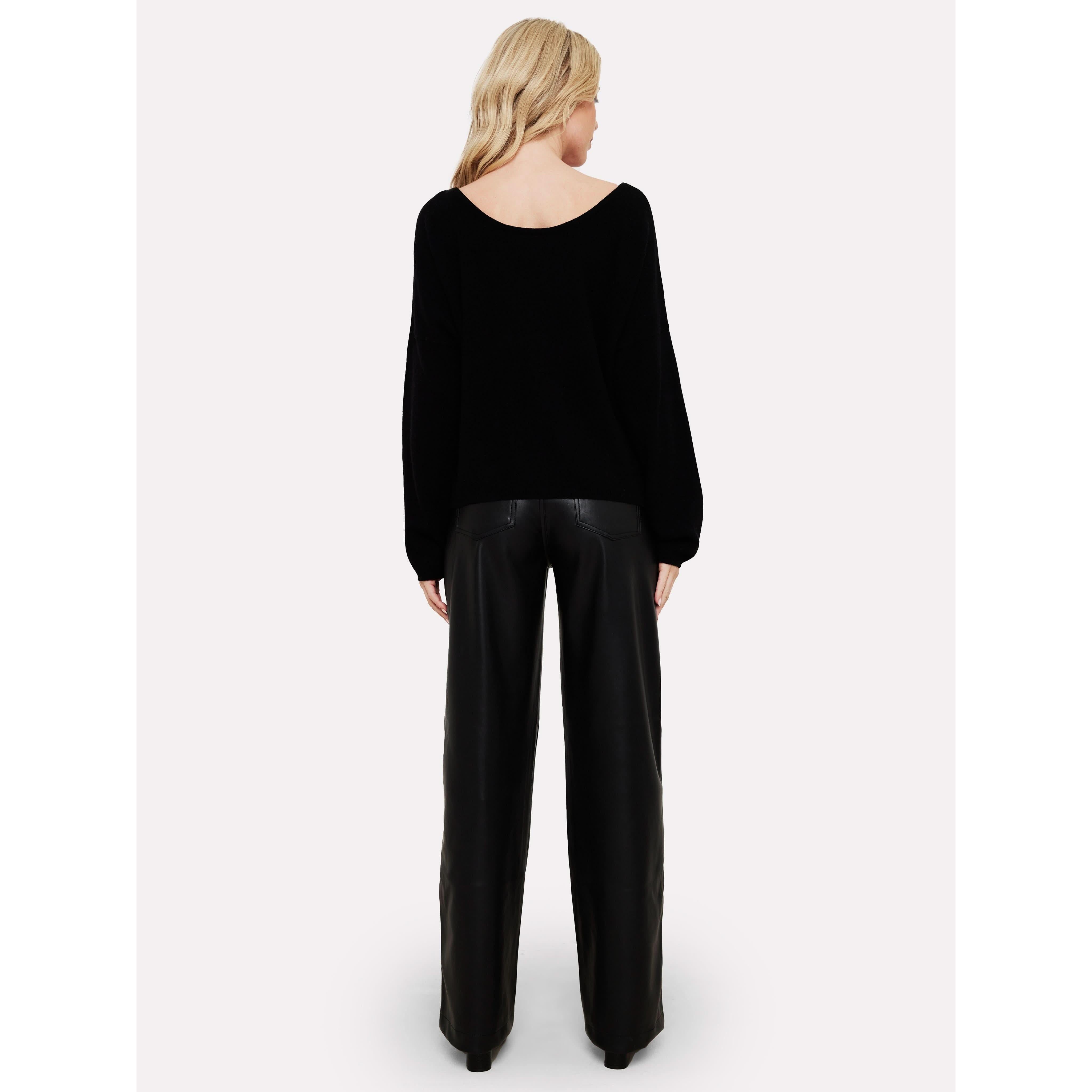 A person with long blonde hair is standing with their back to the camera, dressed in a Brodie Cashmere Rosa Reversible Black sweater and black wide-leg pants, crafted from non-toxic dyes. The outfit is set against a plain white background.