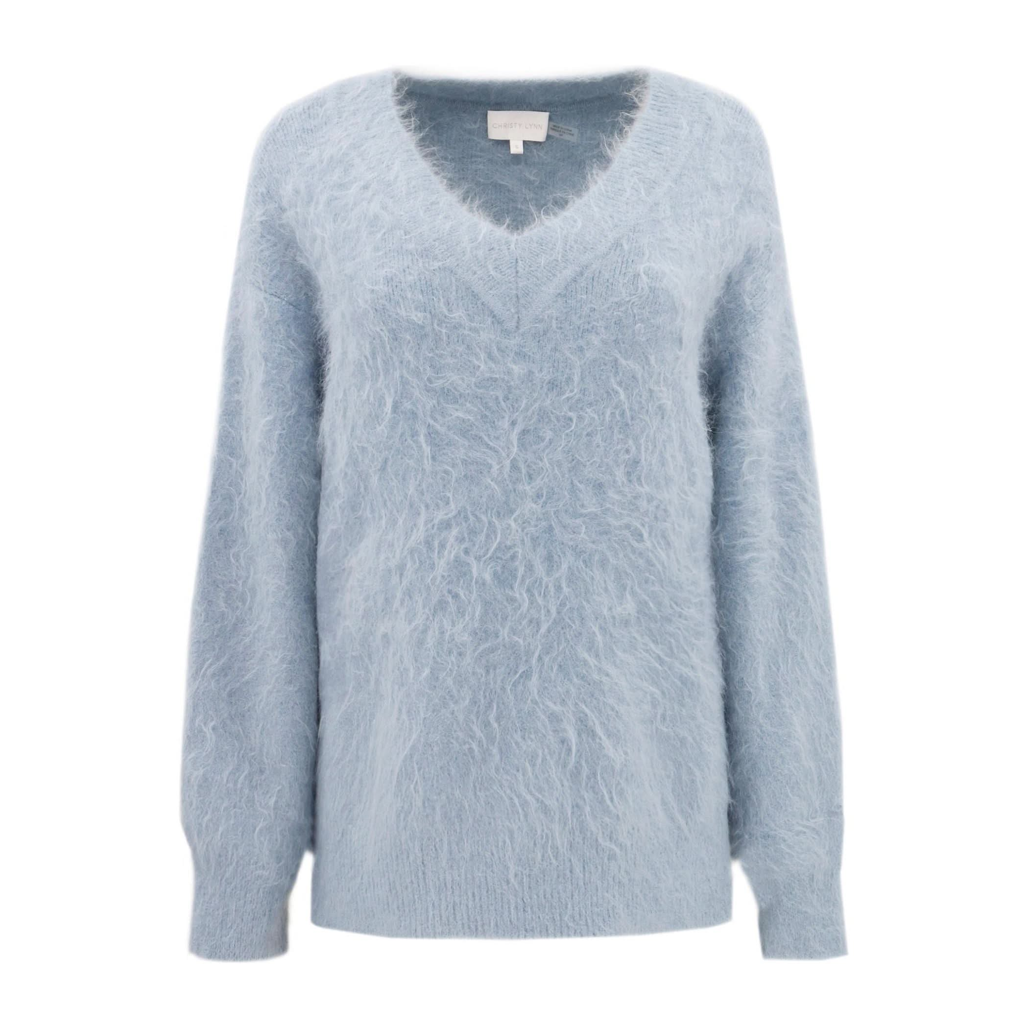 A Christy Lynn Allie Sweater in Dusty Blue, featuring a feminine ruffle along the V-neck and long sleeves, displayed on a plain white background. The soft, textured appearance of the sweater exudes warmth and comfort, reminiscent of the cozy Marfa Top in style.