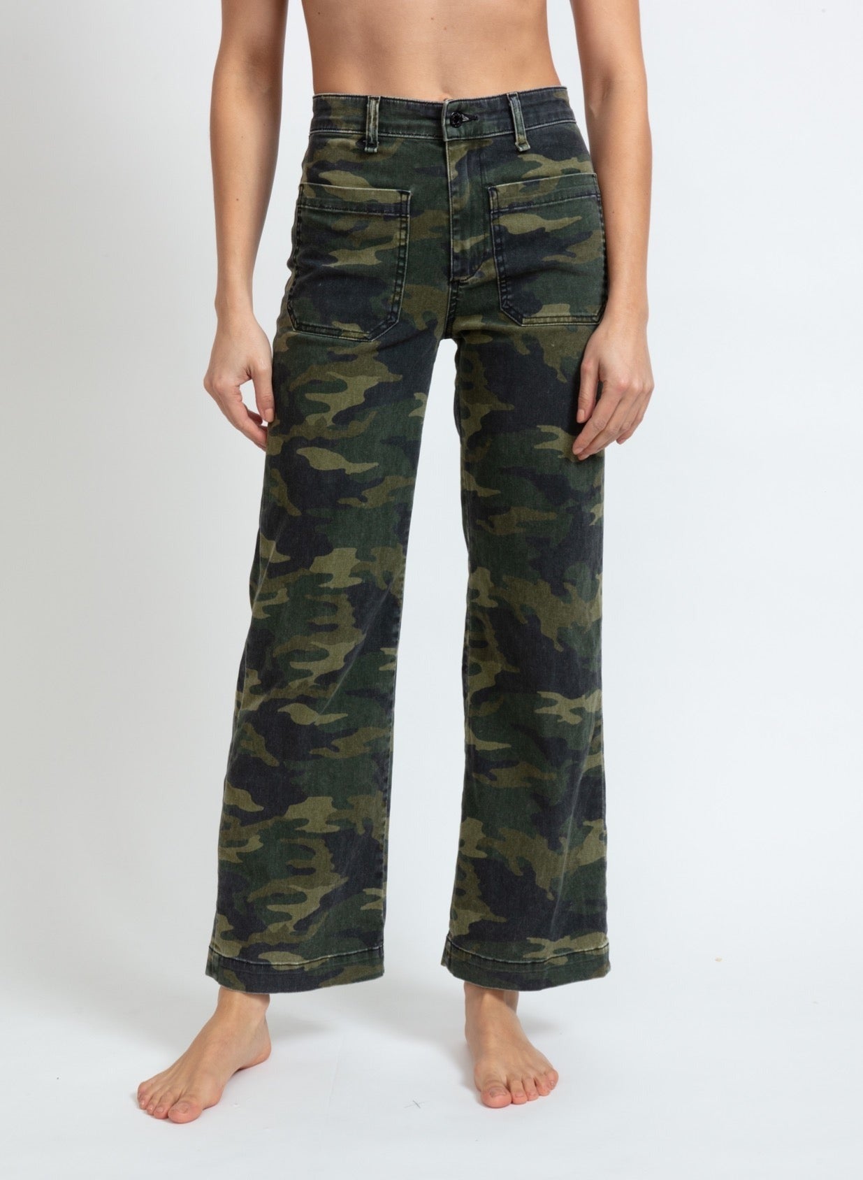 A person is standing barefoot, wearing high-waisted, wide-legged ASKK NY Printed Sailor Pant in camouflage print with front pockets. The image shows the person from the waist down against a plain white background.