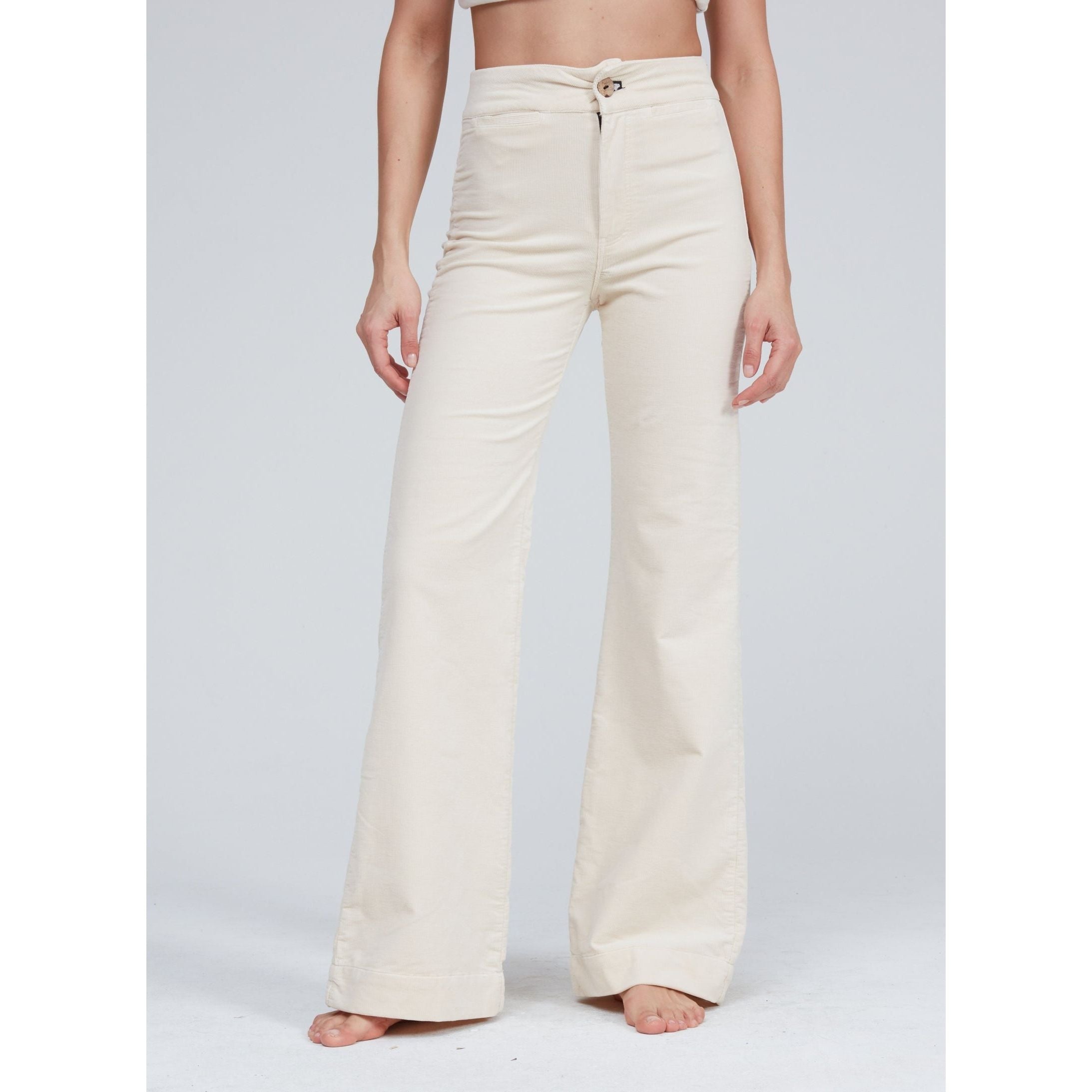 A person stands barefoot against a plain background, wearing the Brighton Wide Leg Bone pants from ASKK NY, crafted from cream-colored Japanese denim. The top part of the body remains unseen in the image.