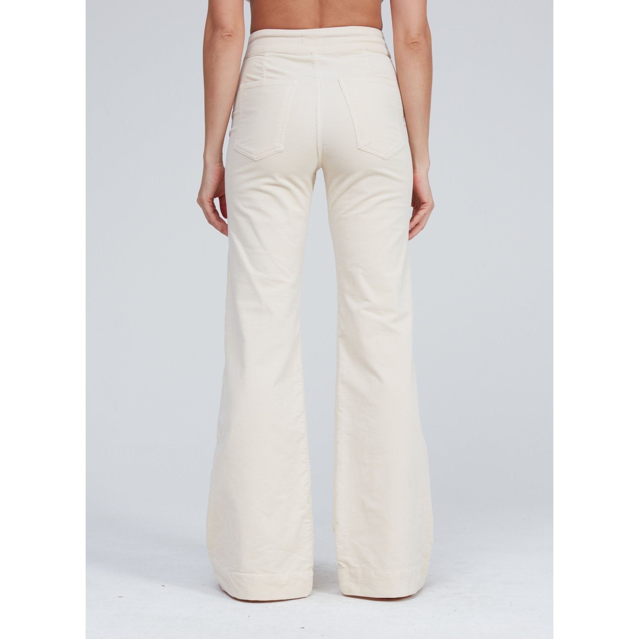 A person is wearing the ASKK NY Brighton Wide Leg Bone pants, which are high-waisted and cream-colored, crafted in Los Angeles. Seen from the back, the wide-leg design includes two back pockets and flares out towards the bottom. The background is a plain light gray.