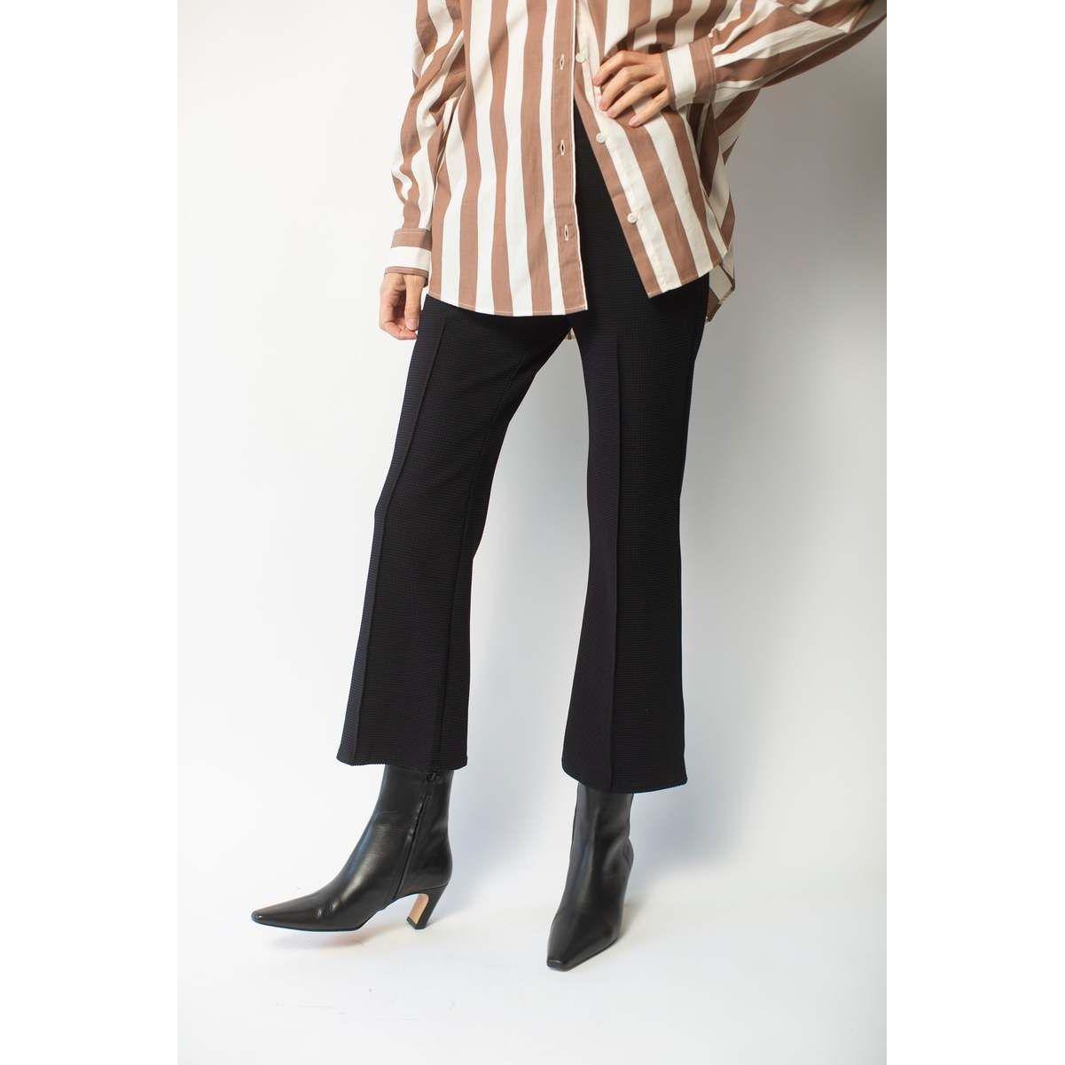 A person is standing against a white background wearing a brown and white striped shirt paired with Donni The Box Weave Stretch Kick Flare pants by Donni and black ankle boots with low heels. Only their legs and torso are visible.