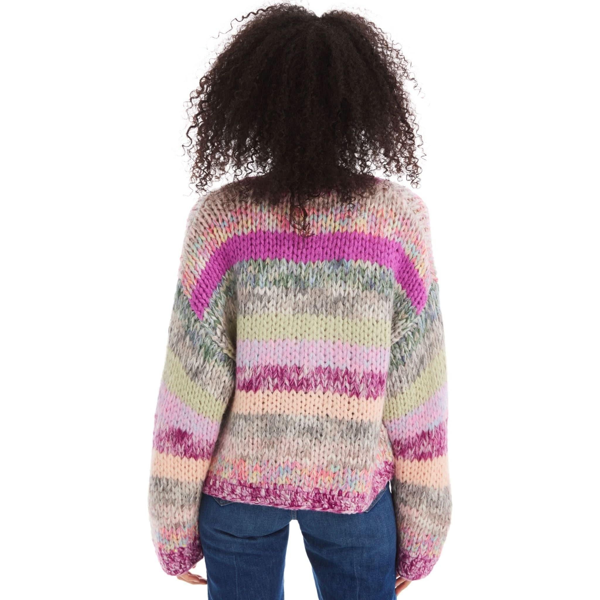 An individual with curly hair is viewed from behind, donning an oversized Allison NY Cropped Jodie Cardigan by Allison. The cardigan features colorful horizontal stripes in shades of pink, purple, beige, and green. They are also wearing blue jeans. This cropped-length sweater requires dry cleaning only.