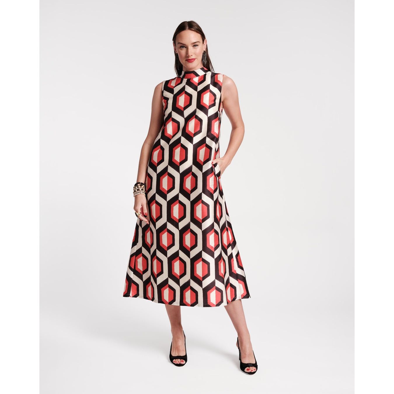 Clad in the Frances Valentine Diplomat Maxi Dress, featuring an Empire Print Jacquard in Oyster and Red, a woman exudes confidence with one hand on her hip. Her look is enhanced with multiple bracelets and black open-toe heels, set against a plain white background.