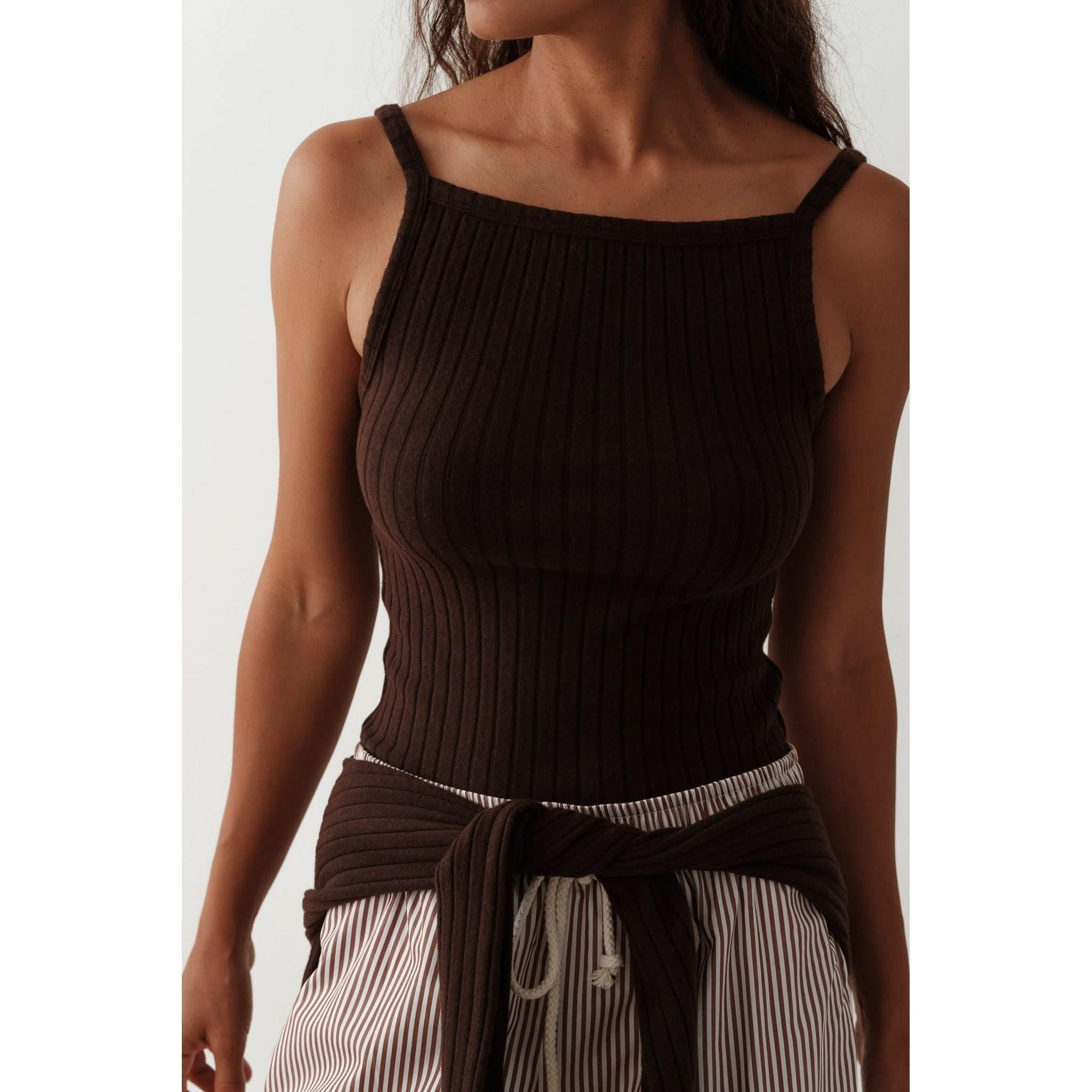 A person wearing a Donni The Sweater Rib Tank Espresso, featuring scalloped edges and paired with striped pants, has a sweater tied around their waist. The photo showcases the cropped fit of the tank against a plain background.