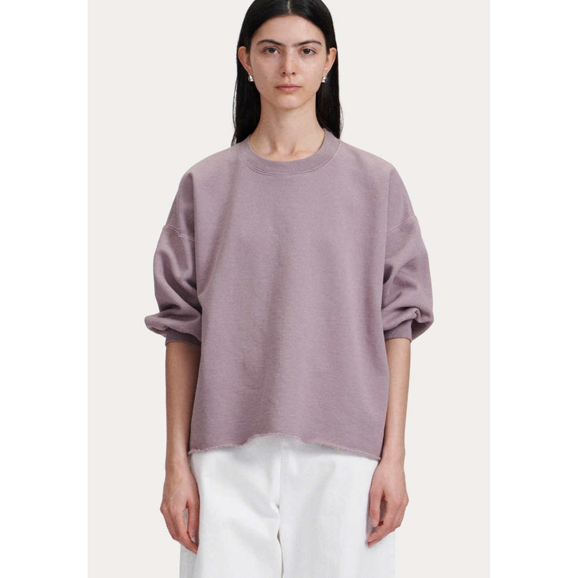 A person with long dark hair is wearing the Rachel Comey Fond Sweatshirt in mauve, featuring balloon sleeves, paired with loose-fitting white pants while standing against a plain background.