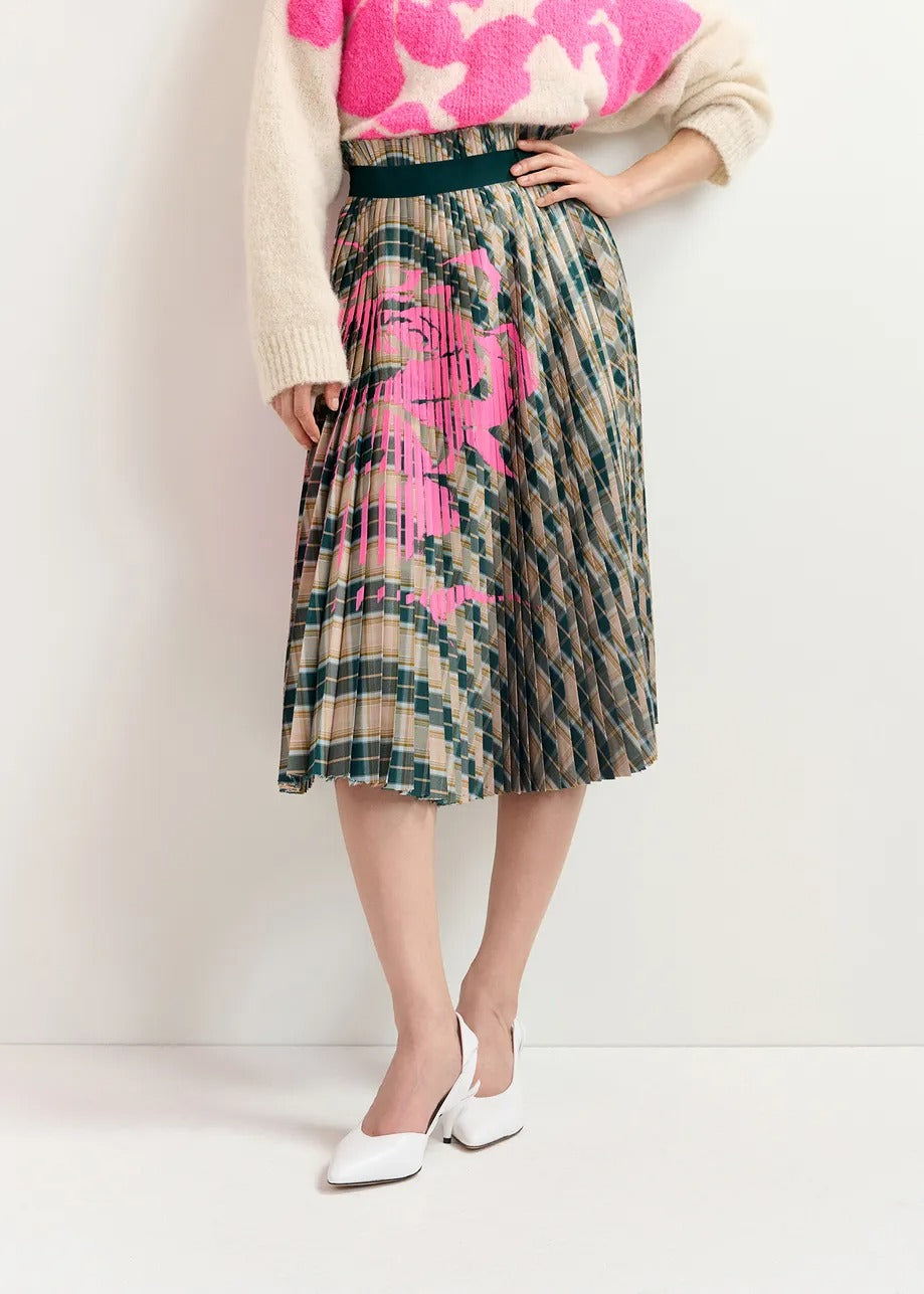 A person is wearing a beige sweater with pink patterns and the Essentiel Antwerp Godess Skirt, a beige and dark green checked pleated skirt with a floral print. They are also sporting white heeled shoes. The image is set against a plain background.