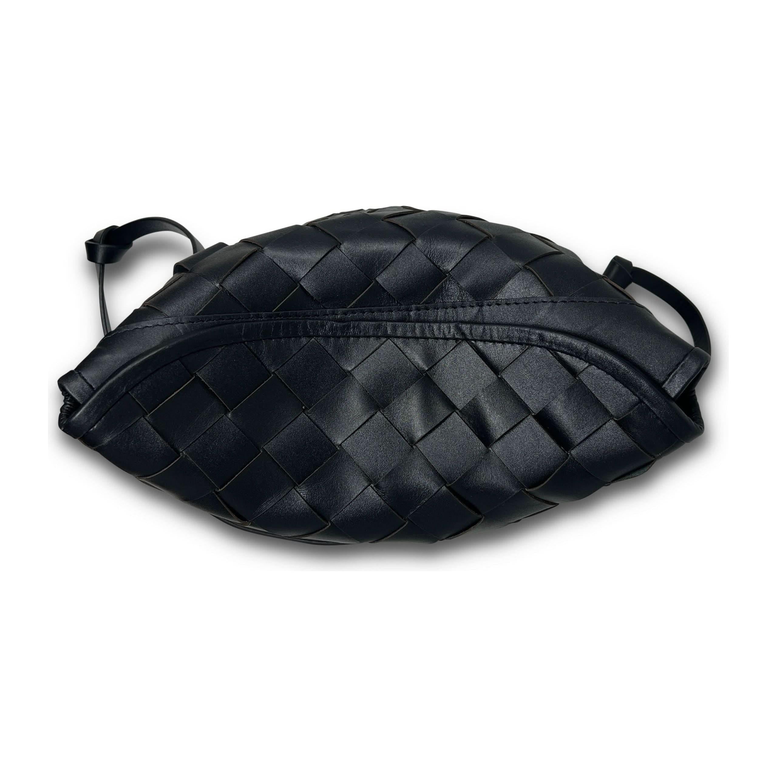 The Kempton & Co Richmond Bucket Bag - Black Threaded Weave is a black leather crossbody bag showcasing a distinctive woven design with overlapping strips. It has a classic, almost oval shape and features a zipper along the top. The attached black strap allows for easy carrying. Its minimal beauty stands out against the completely white background.