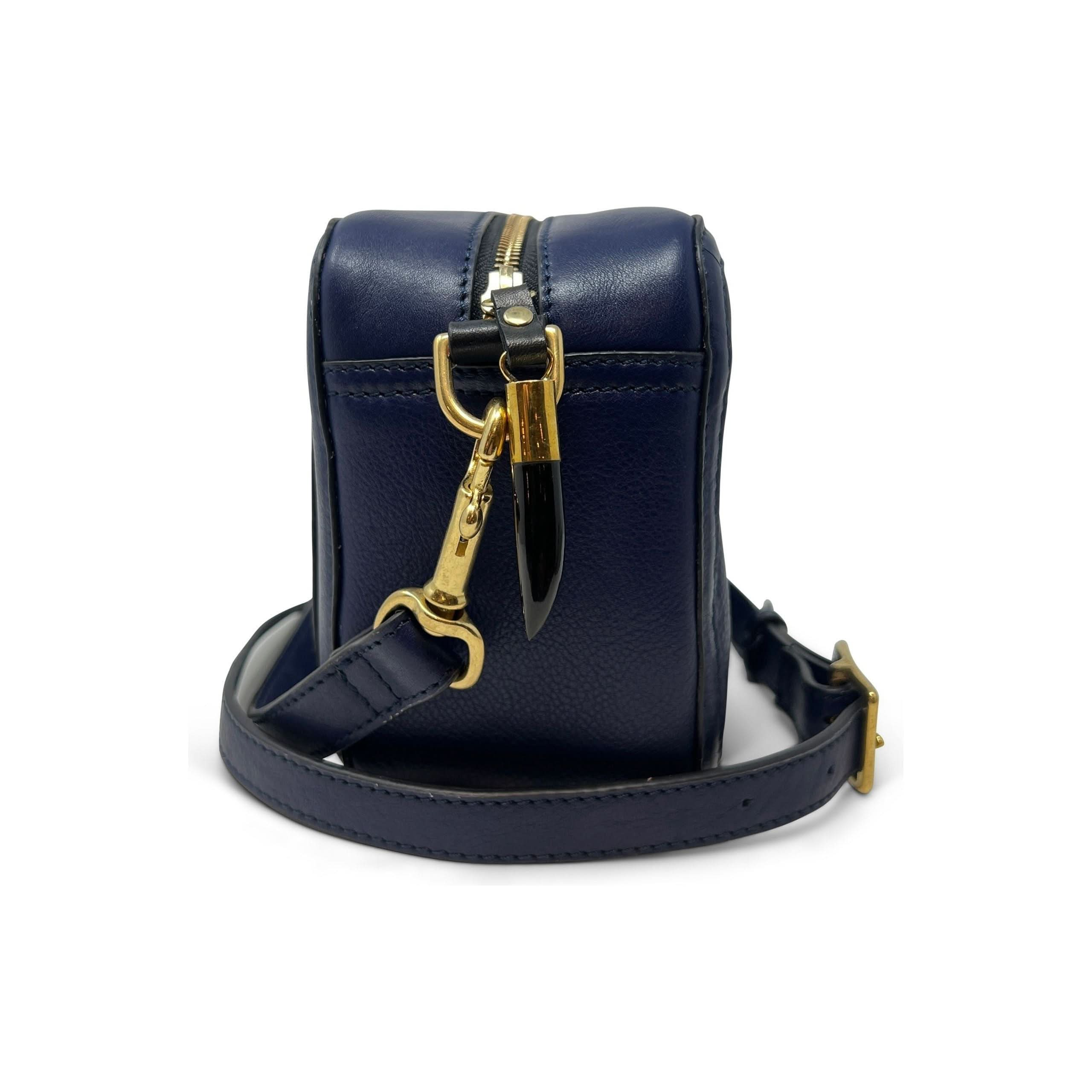 New Style Alert: Introducing the Kempton & Co Amberleigh Crossbody Bag - Pleated Indigo. This small, rectangular navy blue leather handbag from Kempton & Co is shown in profile and features gold hardware. It includes a top zipper, a detachable strap with buckle detail, and a gold clip on the side. With its indigo hue and clean lines reminiscent of vintage travel bags, it exudes a structured look with a smooth finish.