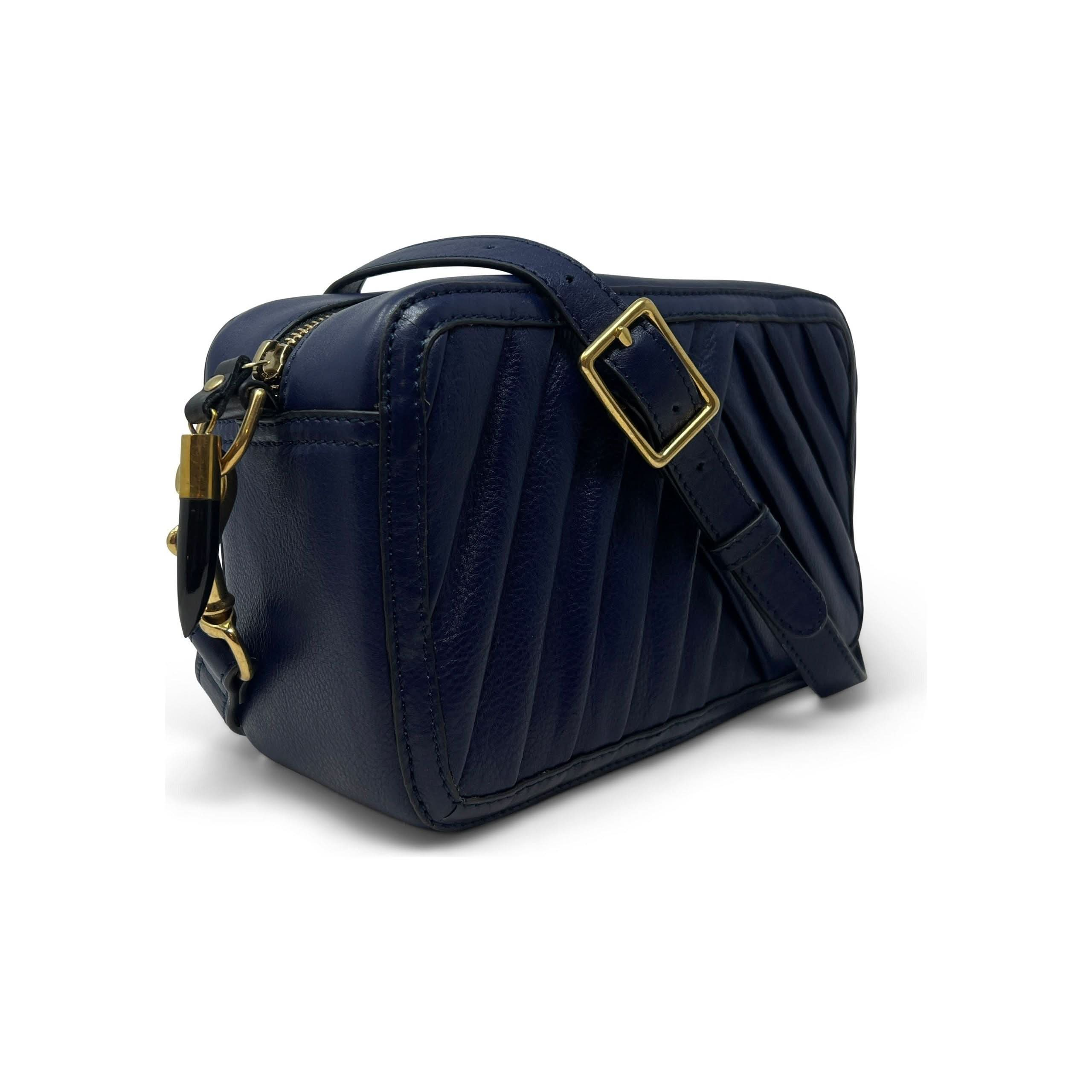 The Kempton & Co Amberleigh Crossbody Bag - Pleated Indigo is a small, rectangular handbag with pleated detailing in an indigo hue. It features a gold-tone buckle on the adjustable shoulder strap and a metallic zipper closure. The bag has a structured, compact design with a modern and elegant appearance. New Style Alert!