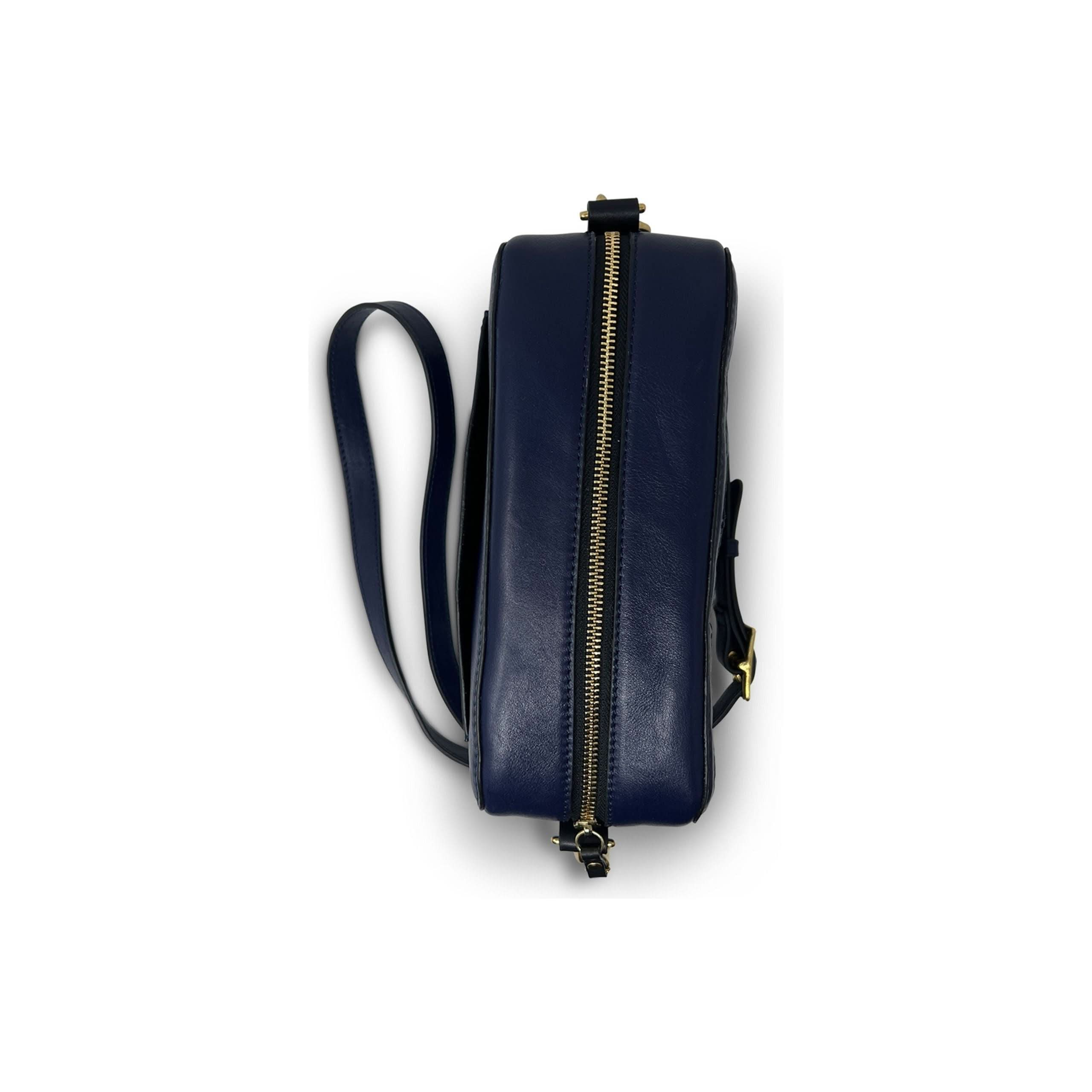 The Kempton & Co Amberleigh Crossbody Bag - Pleated Indigo, reminiscent of vintage travel bags, is shown in a side profile against a white background. The navy blue leather bag features a gold zipper along the top and a partially visible leather strap, giving it a sleek and modern appearance. New Style Alert!