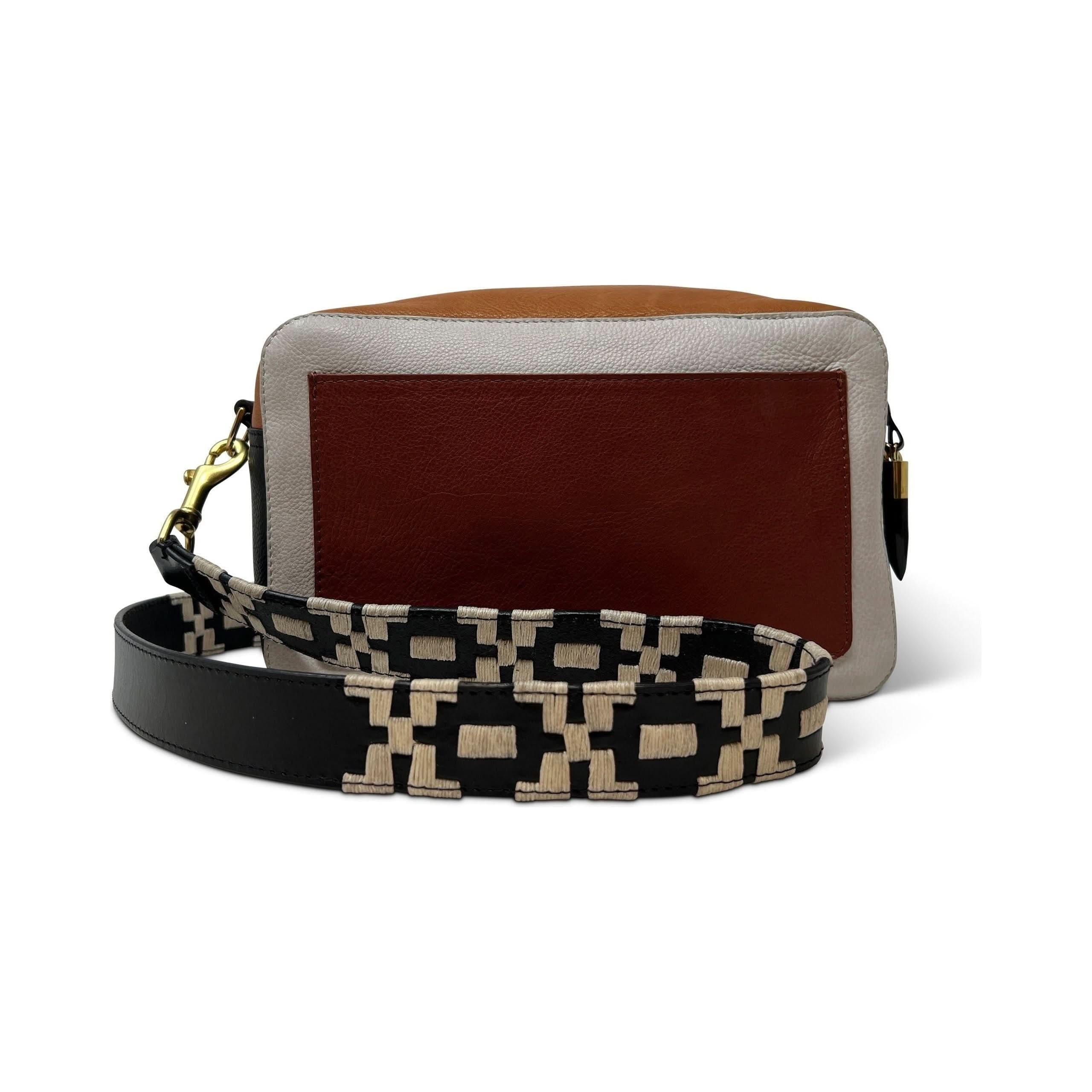 A rectangular, brown and beige Kempton & Co Amberleigh Crossbody Bag - Burnt Henna Brogue is displayed against a white background. The bag features a front pocket and has a detachable crossbody strap with a geometric black and beige pattern, complementing its leather woven exterior.