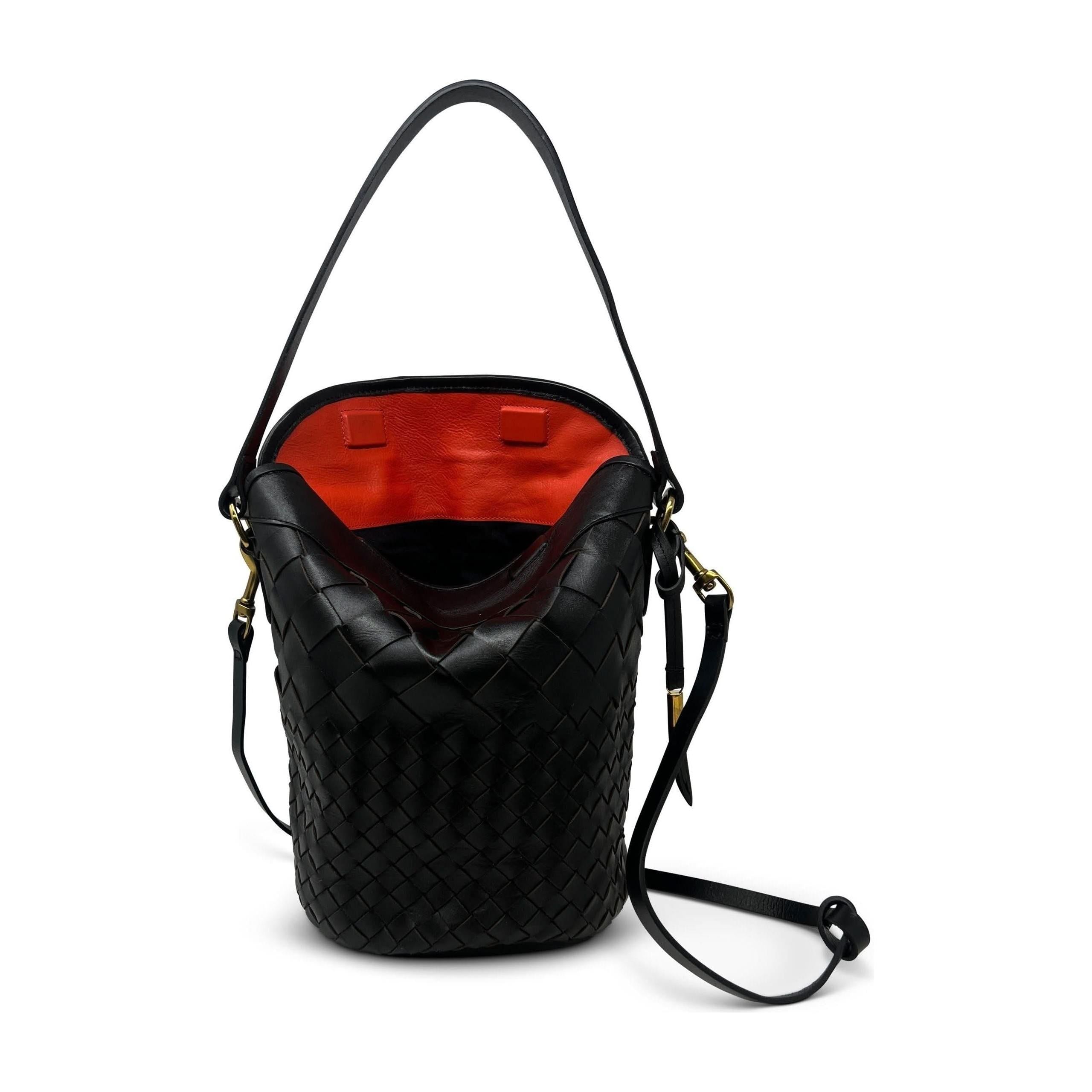 The Kempton & Co Richmond Bucket Bag in Black Threaded Weave, adorned with gold-tone hardware, is showcased with its top handle and detachable shoulder strap. The top is open, unveiling a vibrant red interior that complements the bag's classic and sleek modern design.