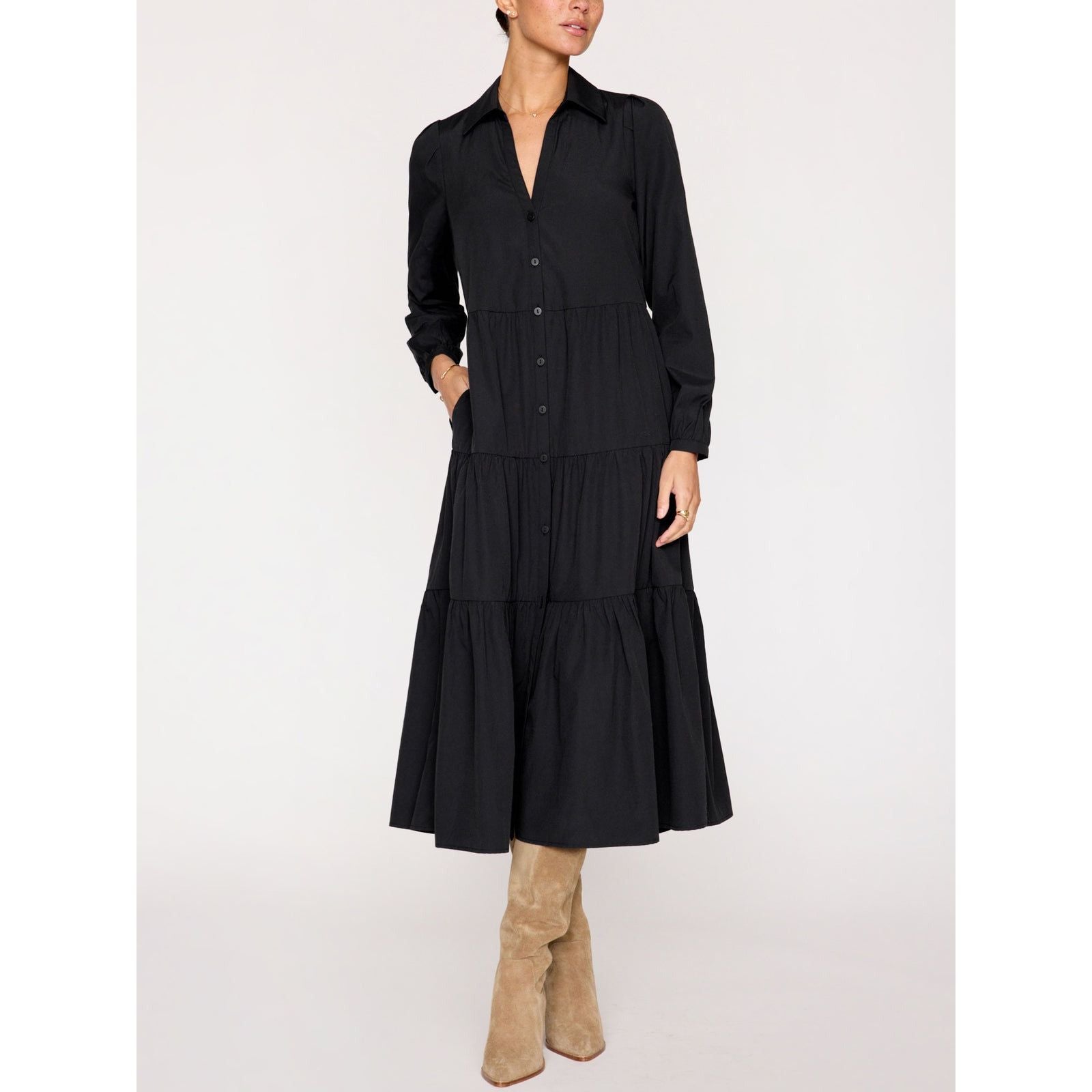 A person is wearing the Brochu Walker Long Sleeve Havana Dress in black, a button-up tiered dress with puff sleeves that reaches mid-calf. They are also wearing tan suede knee-high boots. The background is plain and light-colored.