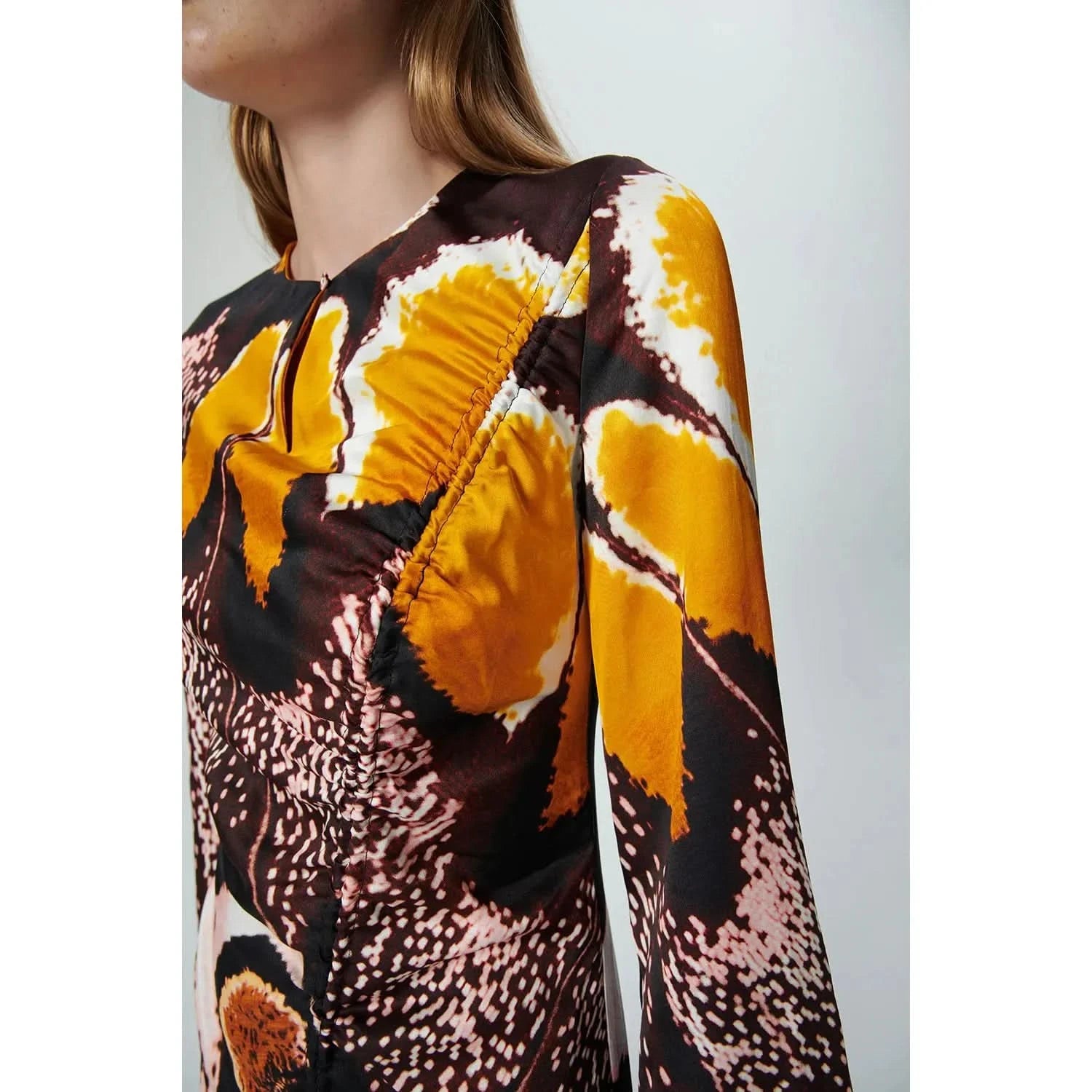 Close-up of a person wearing the Chufy Orchid Maxi Dress, crafted from sustainable fabric and adorned with a vibrant abstract pattern in yellow, brown, white, and pink accents. This long-sleeved dress by Chufy features ruched detail on the chest, with the person's face partially out of frame.