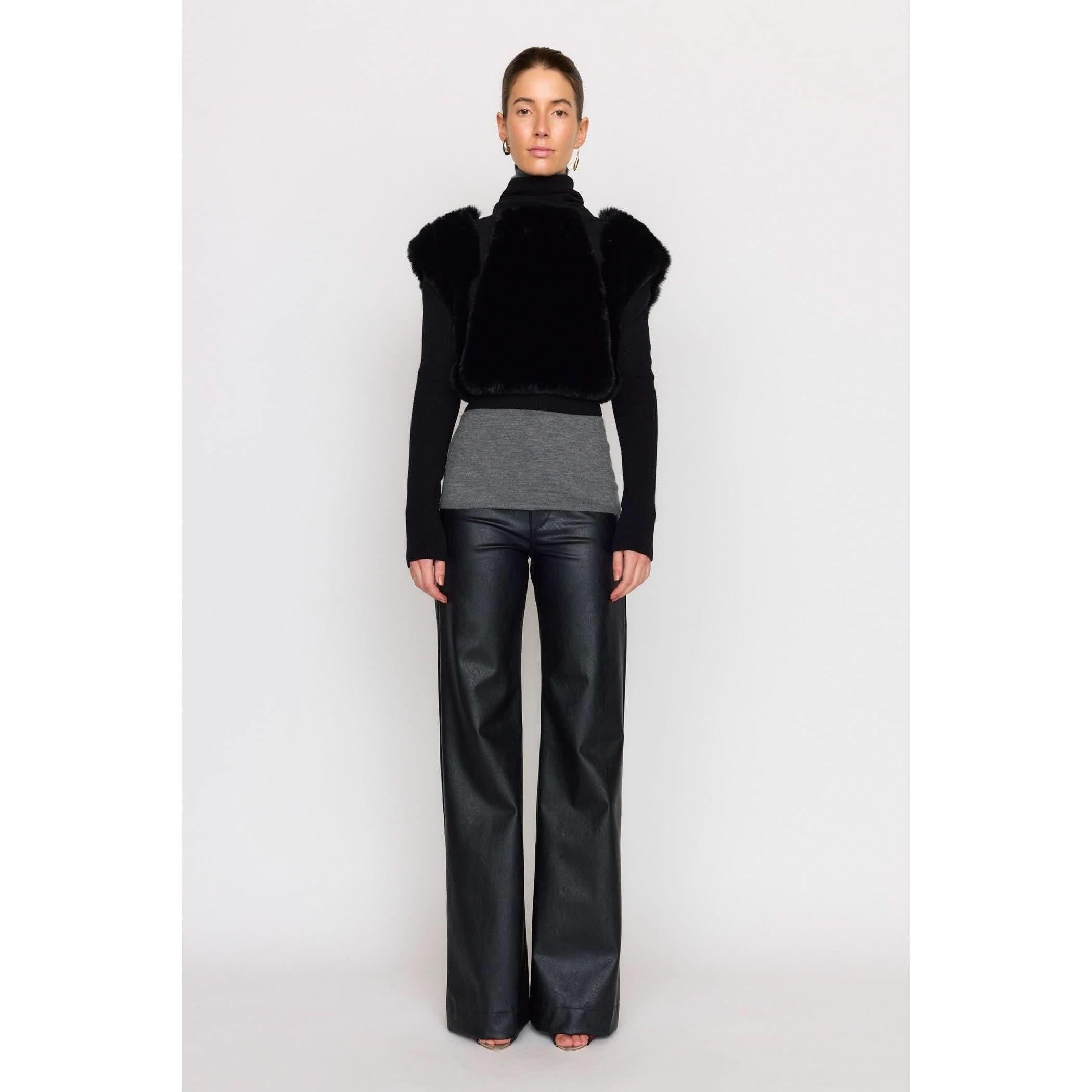 A person stands against a plain background wearing the Christy Lynn Criselle Knit in black, complemented by a long-sleeve black shirt and wide-leg vegan leather pants. Their hair is tied back, and they're adorned with small hoop earrings.