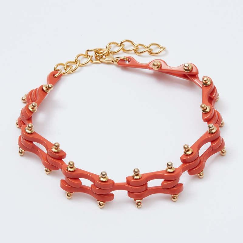 The Rachel Comey Bedford Chocker by Rachel Comey is a stylish accessory featuring interlocking red segments adorned with small gold-tone bead accents, all connected by a gold chain with an adjustable clasp. The choker rests on a plain white background.