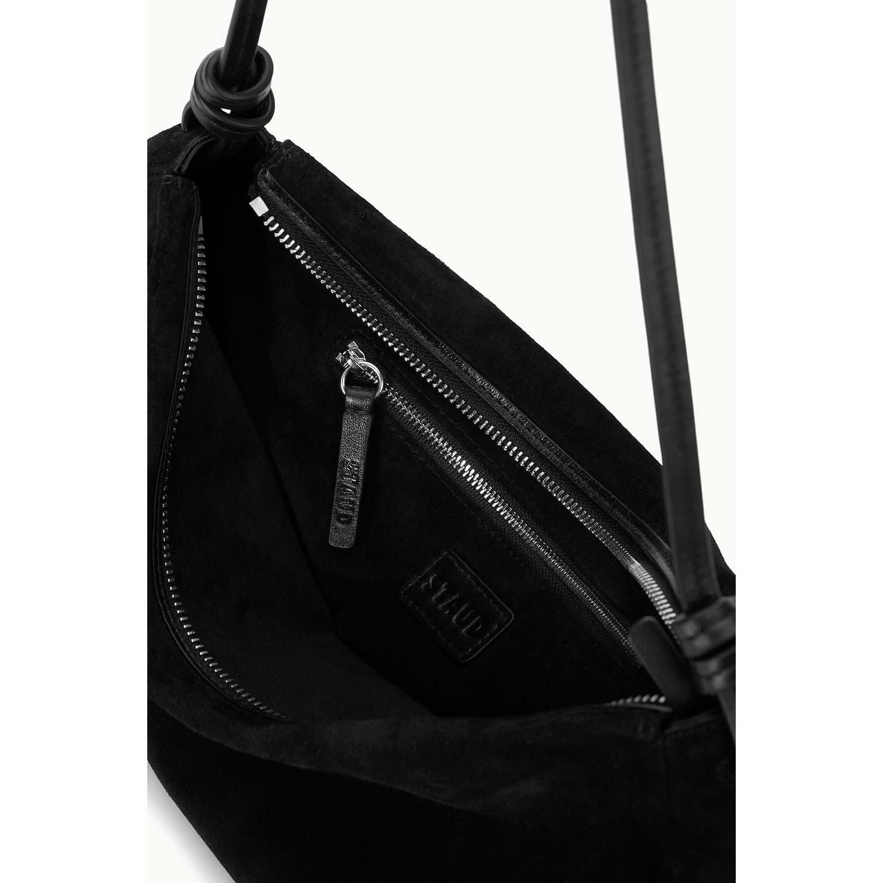 Close-up of an open Staud Wally Bag Black, reminiscent of a leather shoulder bag, showcasing its interior. The bag features a zippered pocket with a leather pull tab and a logo patch. Two black handles are visible at the top, and the fabric appears soft and textured.