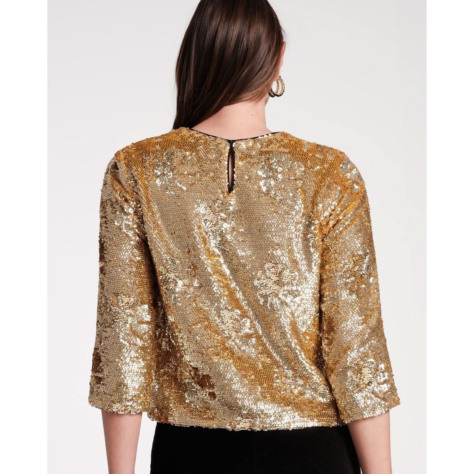 A woman with long brown hair is elegantly dressed in a Frances Valentine Taylor Sequin Top Floral, showcasing a stunning evening look with shimmering gold sequins and delicate floral appliques on the elbow-length sleeves, viewed from the back against a plain background.