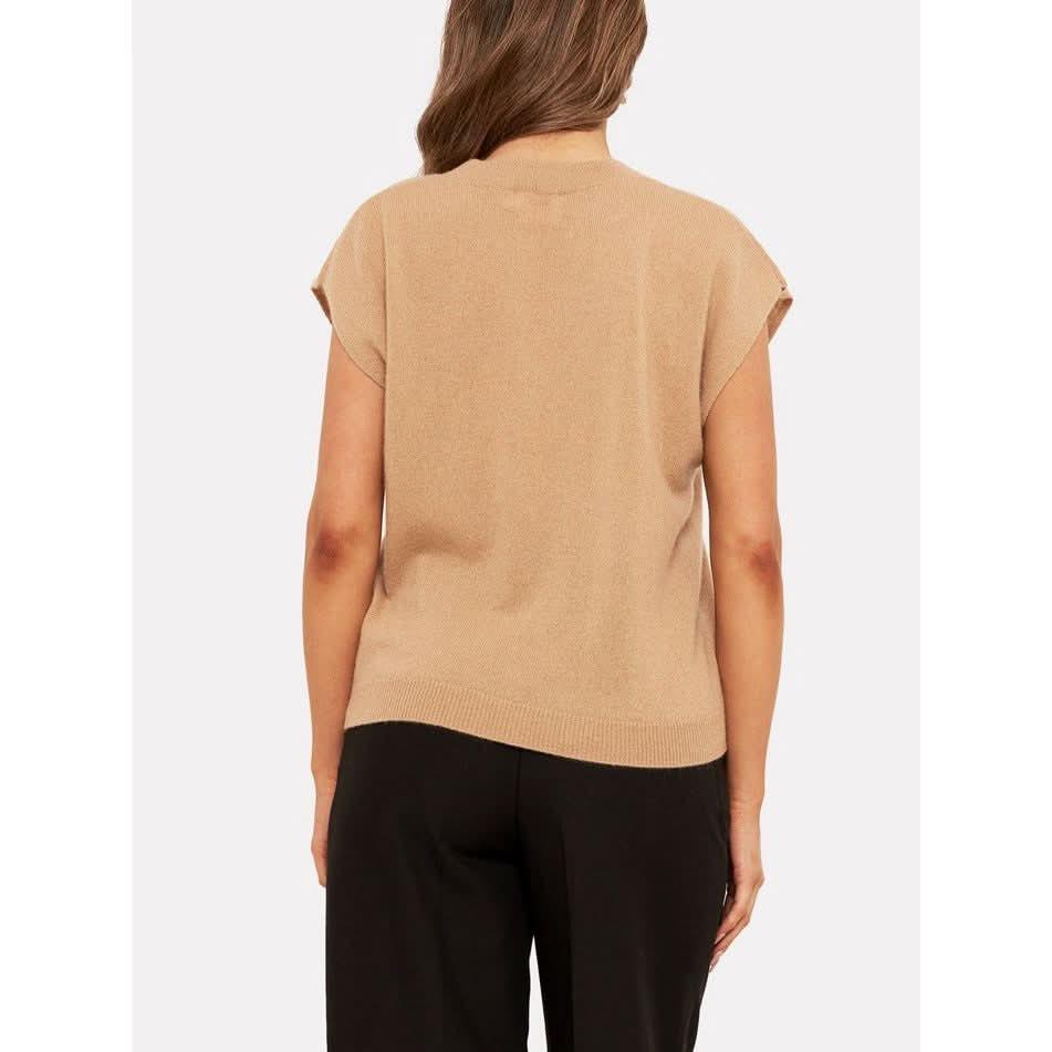 A person with long hair is wearing a camel Brodie Cashmere Tabby cashmere tank and black pants. They are facing away, standing against a plain white background.