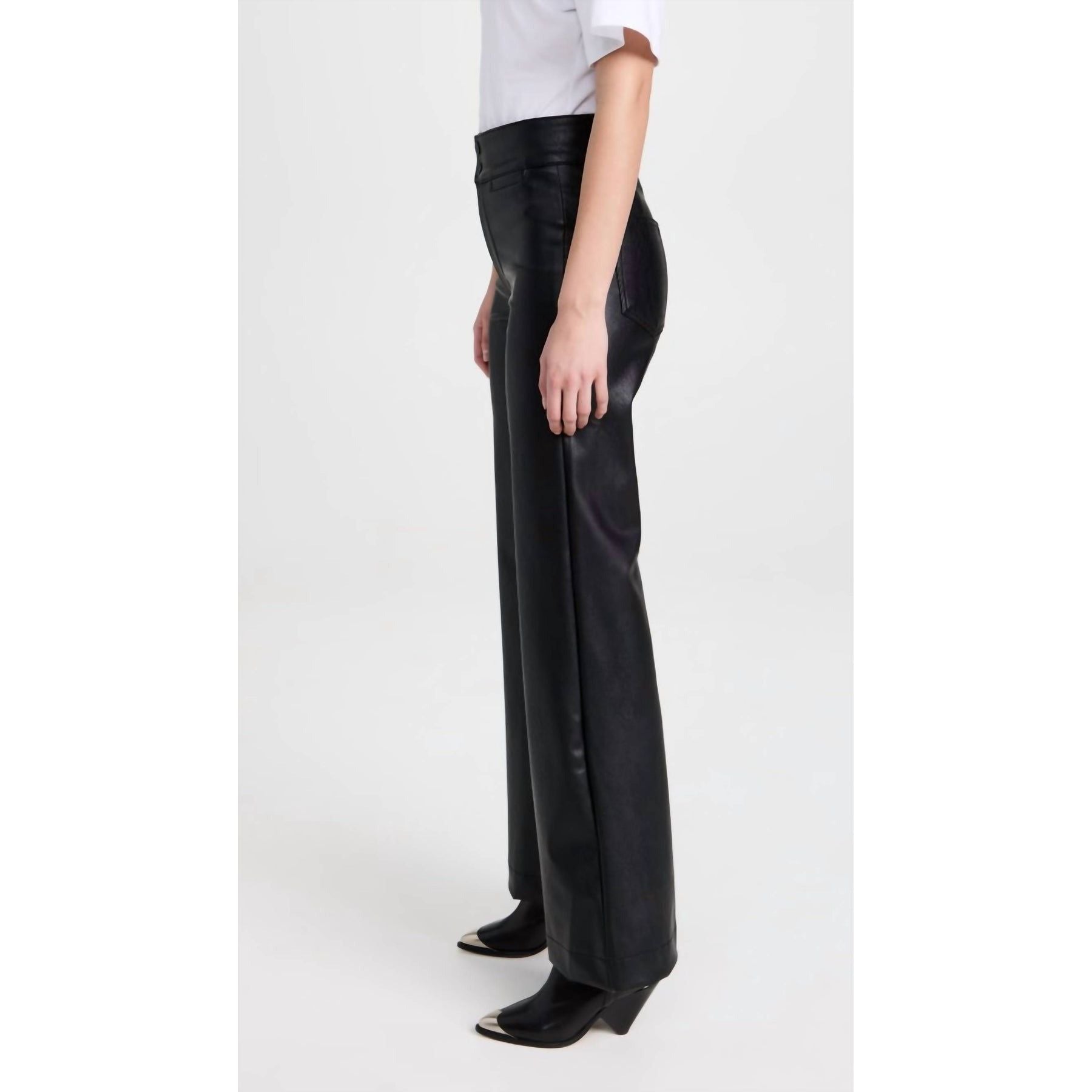 A person in a white shirt and ASKK NY Vegan Brighton Wide Leg Black pants stands sideways. Their ensemble is complemented by black pointed-toe shoes with a wedge heel, set against a plain white background, exuding a sleek modern vibe akin to high-rise slim fit jeans.