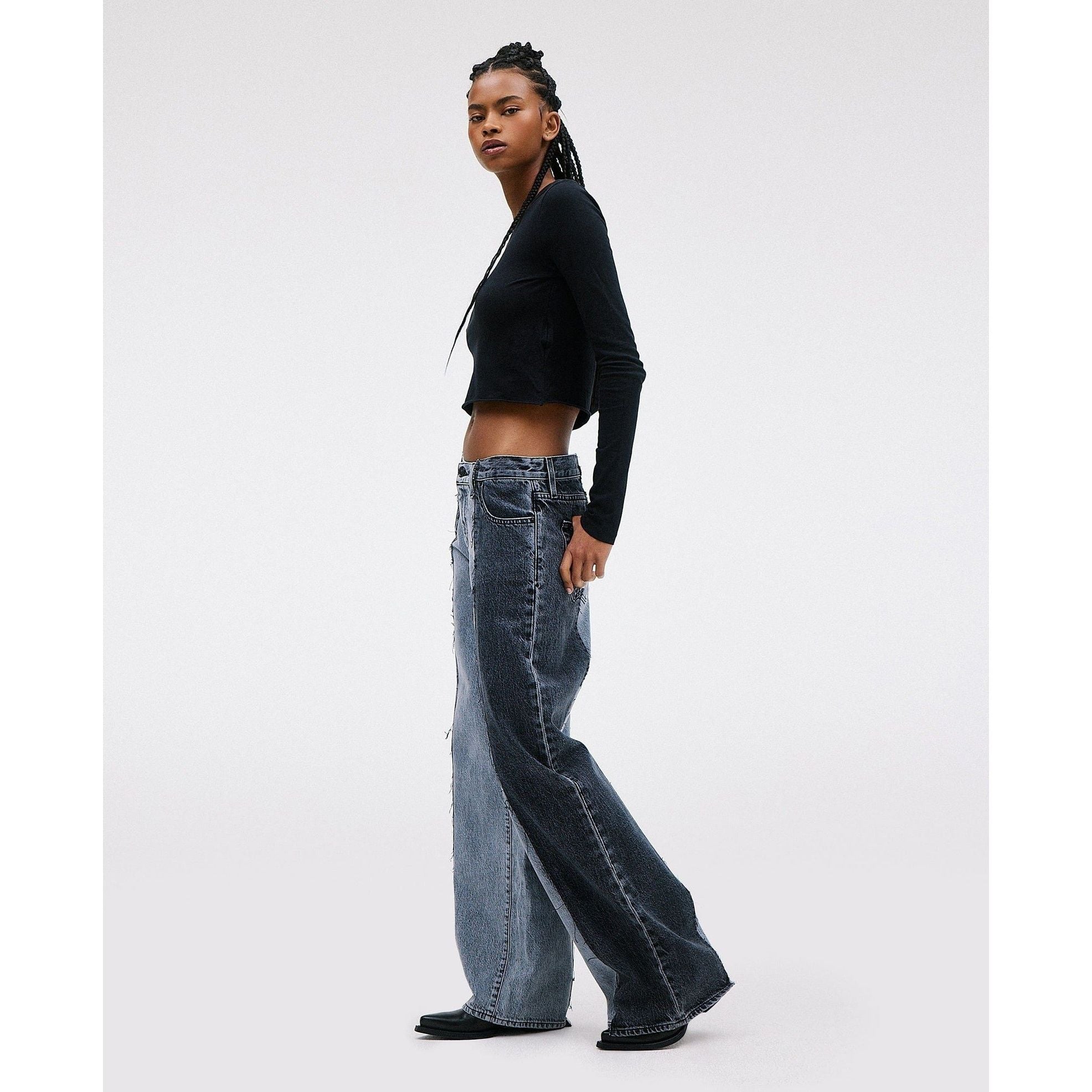 A person stands in profile against a plain background, wearing the SLVRLAKE RE-Work Mica Panel Lunar Eclipse top and high-rise, crafted denim jeans with cropped wide legs. The outfit is casual and stylish, complemented by the person's hair elegantly styled in braids.