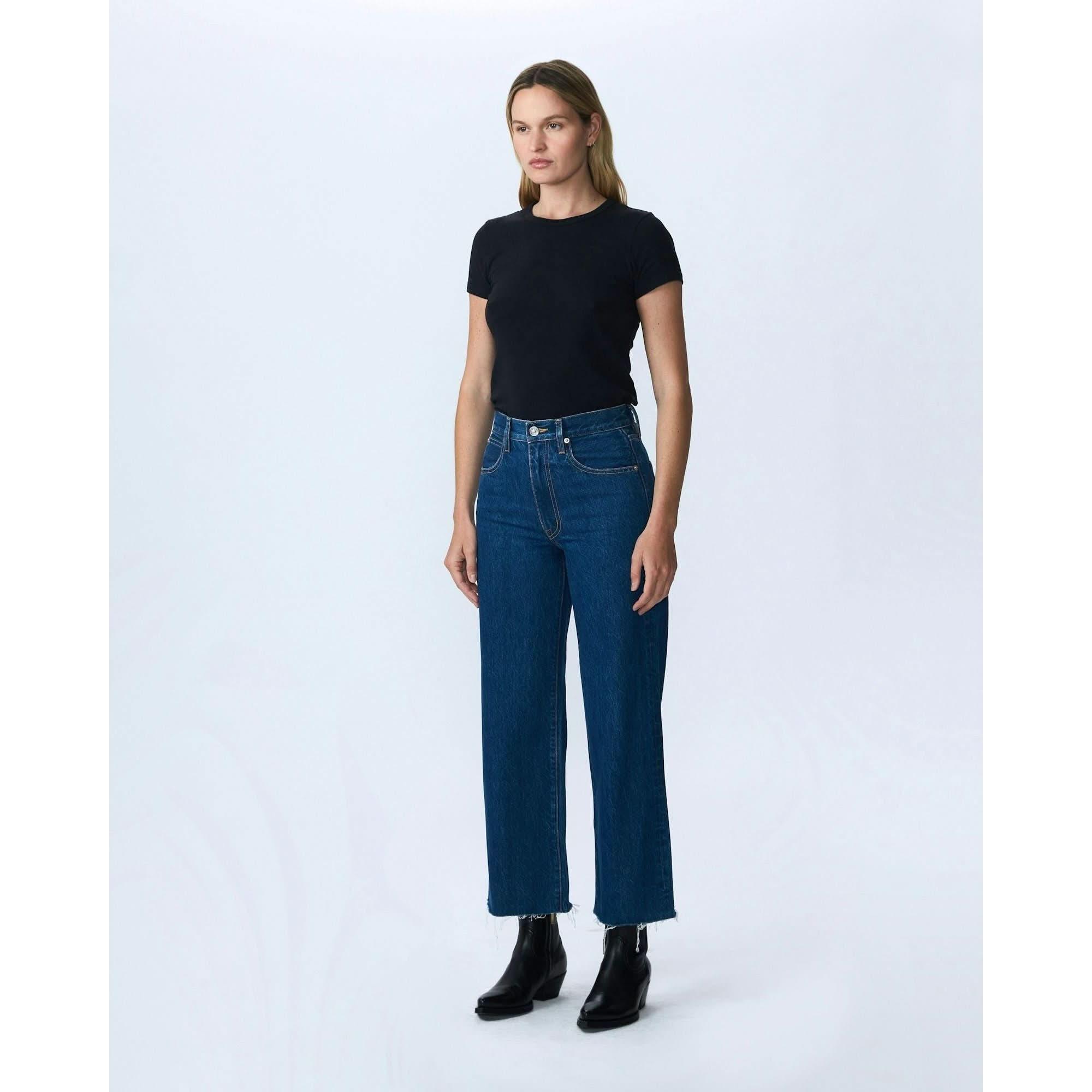 A woman stands against a plain white background, wearing the Slvrlake Denim Grace Crop Revolution, which features a stylish wide leg and cropped length. Her black t-shirt and ankle boots complement the high-rise style of her jeans by SLVRLAKE. With a neutral expression, she gazes slightly to the side.