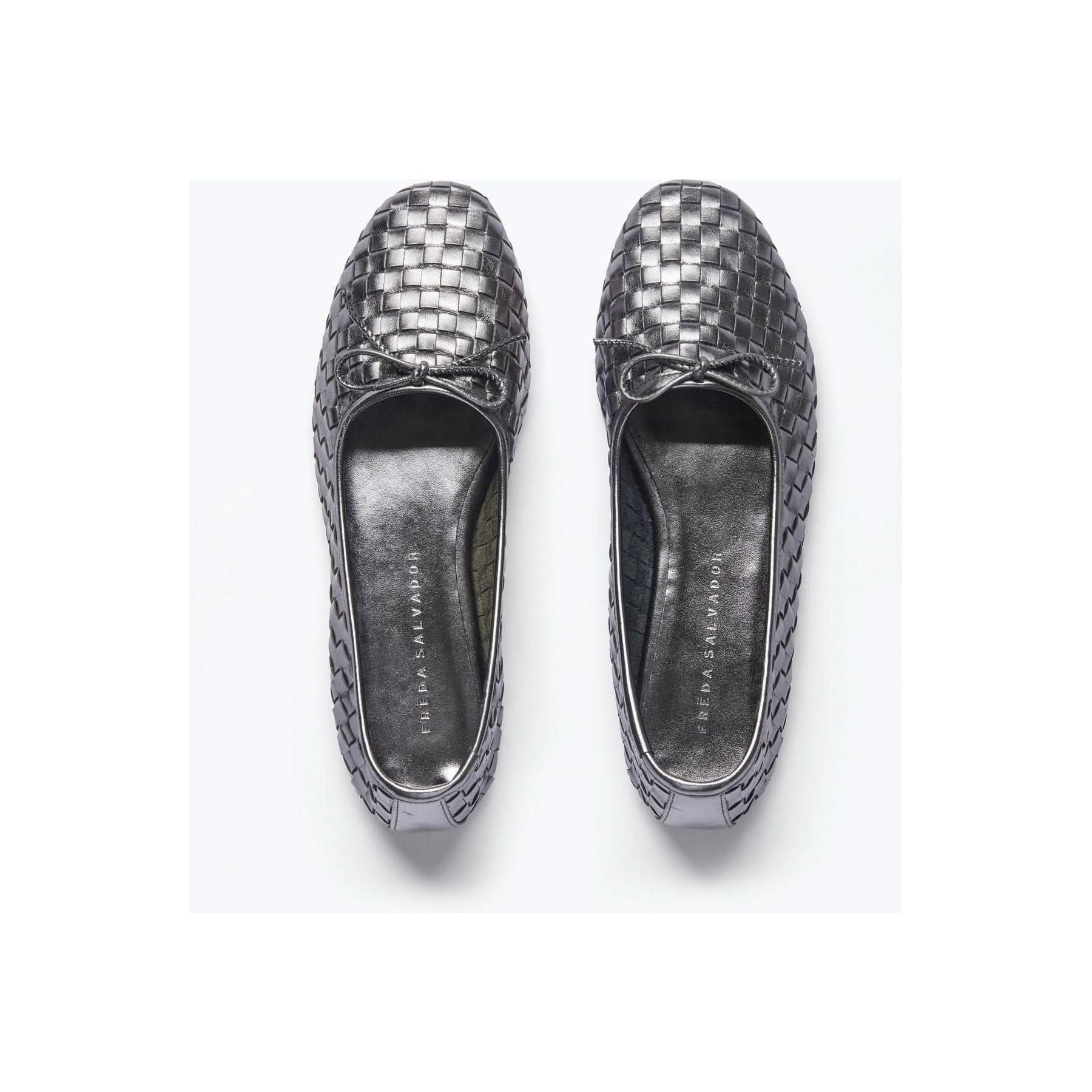 Top view of a pair of Freda Salvador Roma Round Toe Ballet Flats in gunmetal woven calf leather, featuring small bows on the front. Expertly crafted to Leather Working Group standards, the shoes are positioned side by side on a light background.